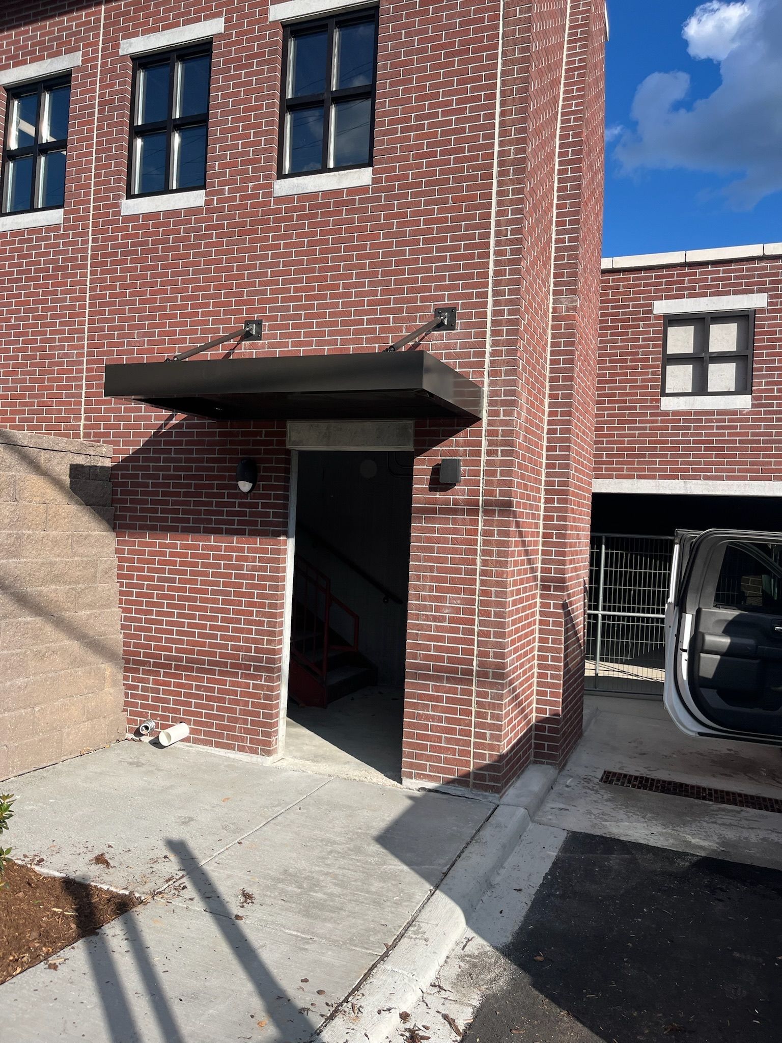 Brick building with entrance under a black awning. Concrete walkway and sky visible.