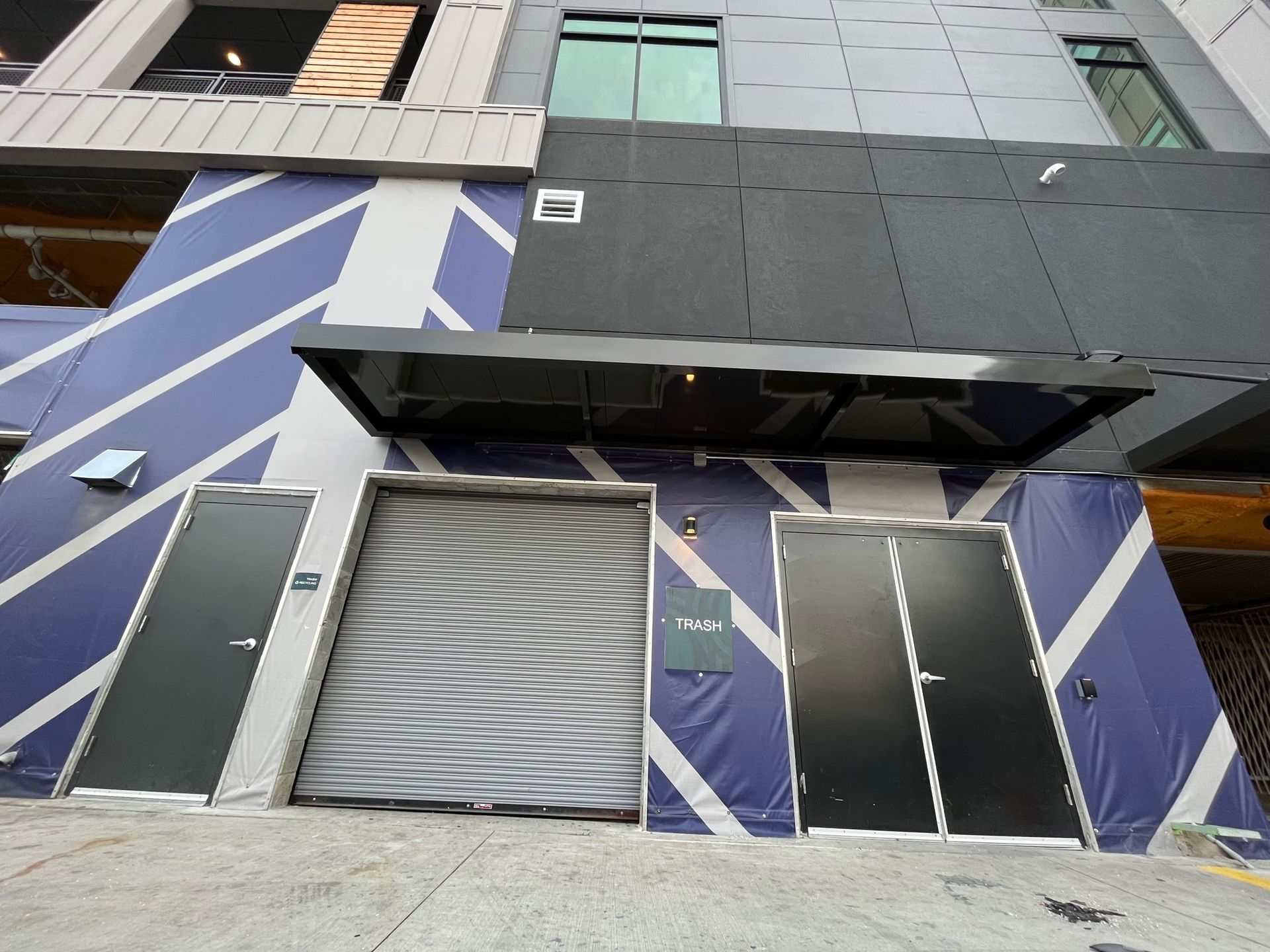 Exterior view of building entrance with a roll-up door and two black doors on a blue-and-white patterned wall.