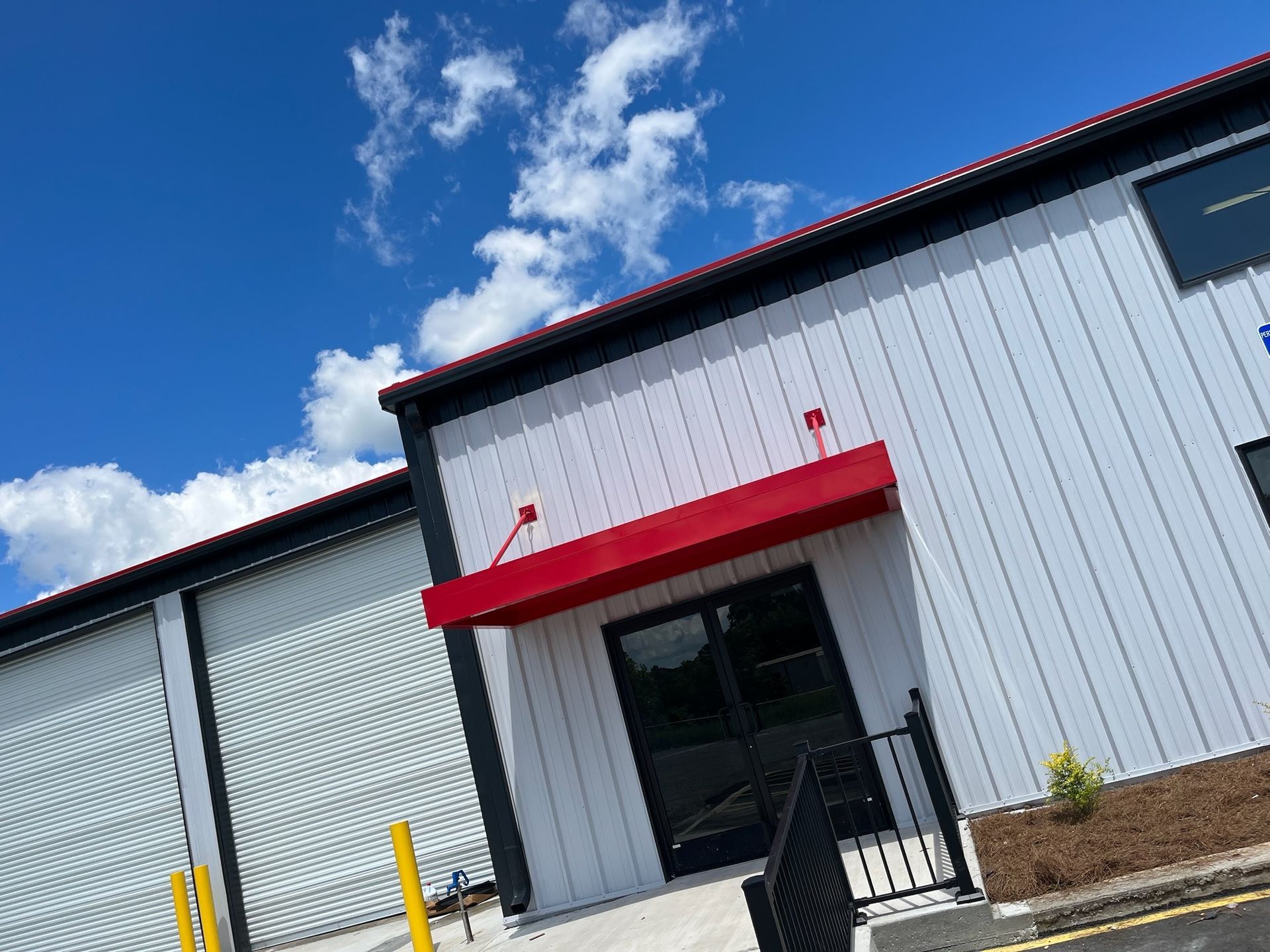 Exterior of a commercial building with a red awning. White and gray metal siding, blue sky, and a small black railing.