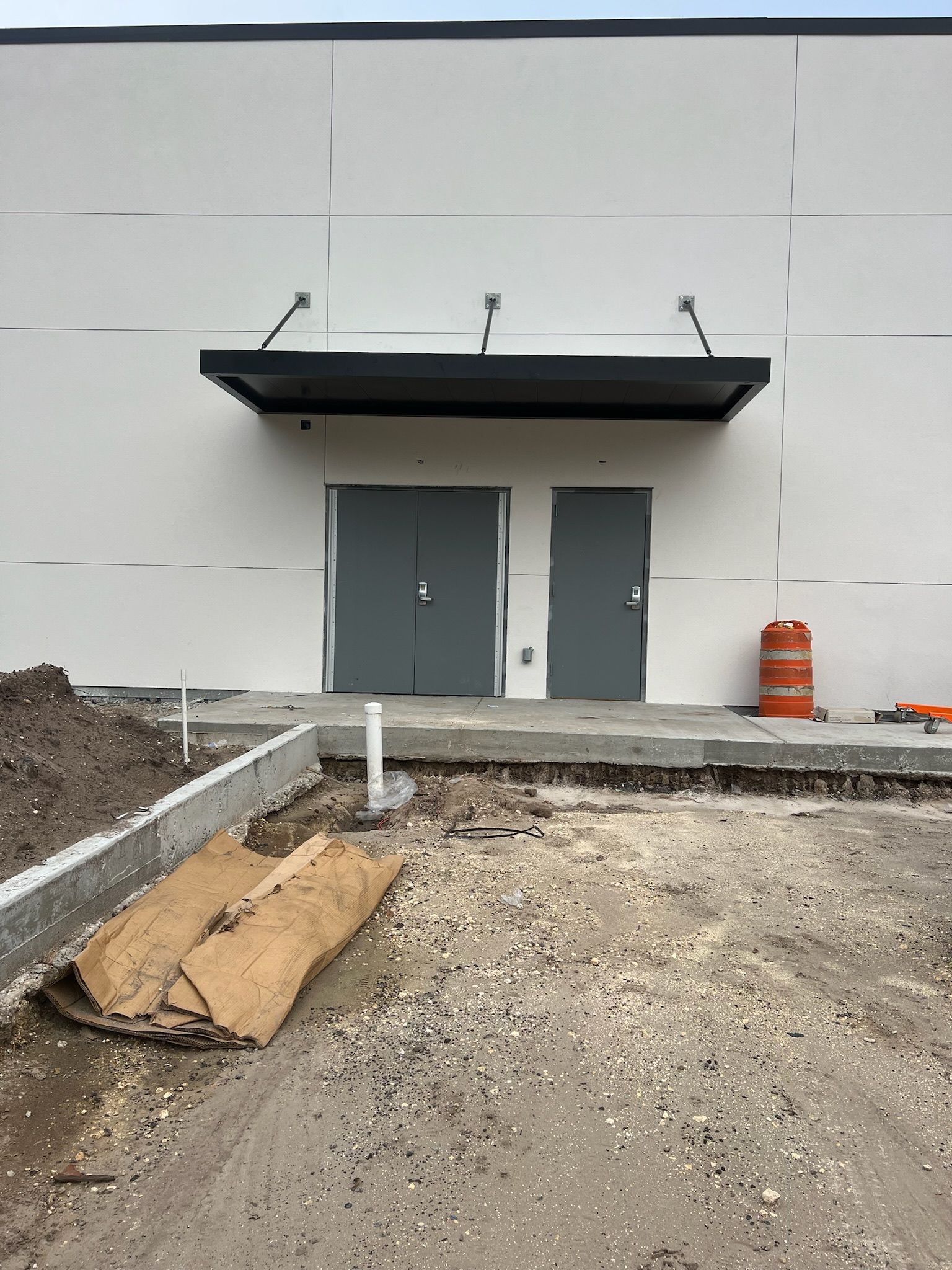 Exterior of a building with two grey doors under a black awning. Construction materials in the foreground.