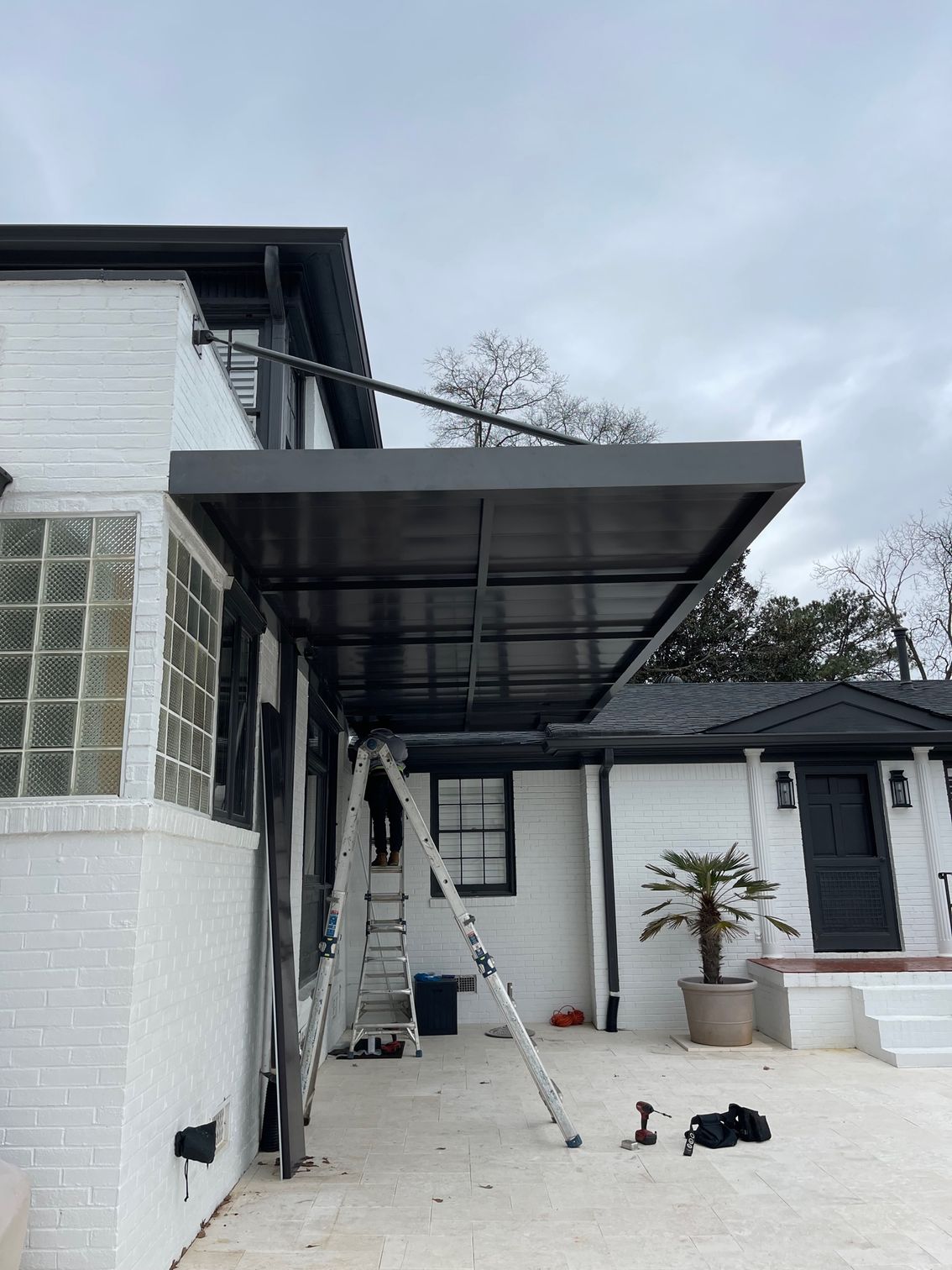 Exterior view of a white brick building with a dark gray awning. A person stands on a ladder.
