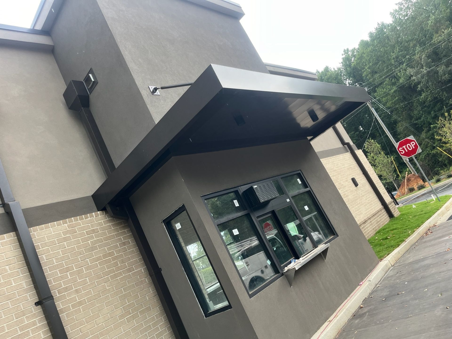 Drive-through of a building with dark gray exterior, windows, and awning. A stop sign is visible.