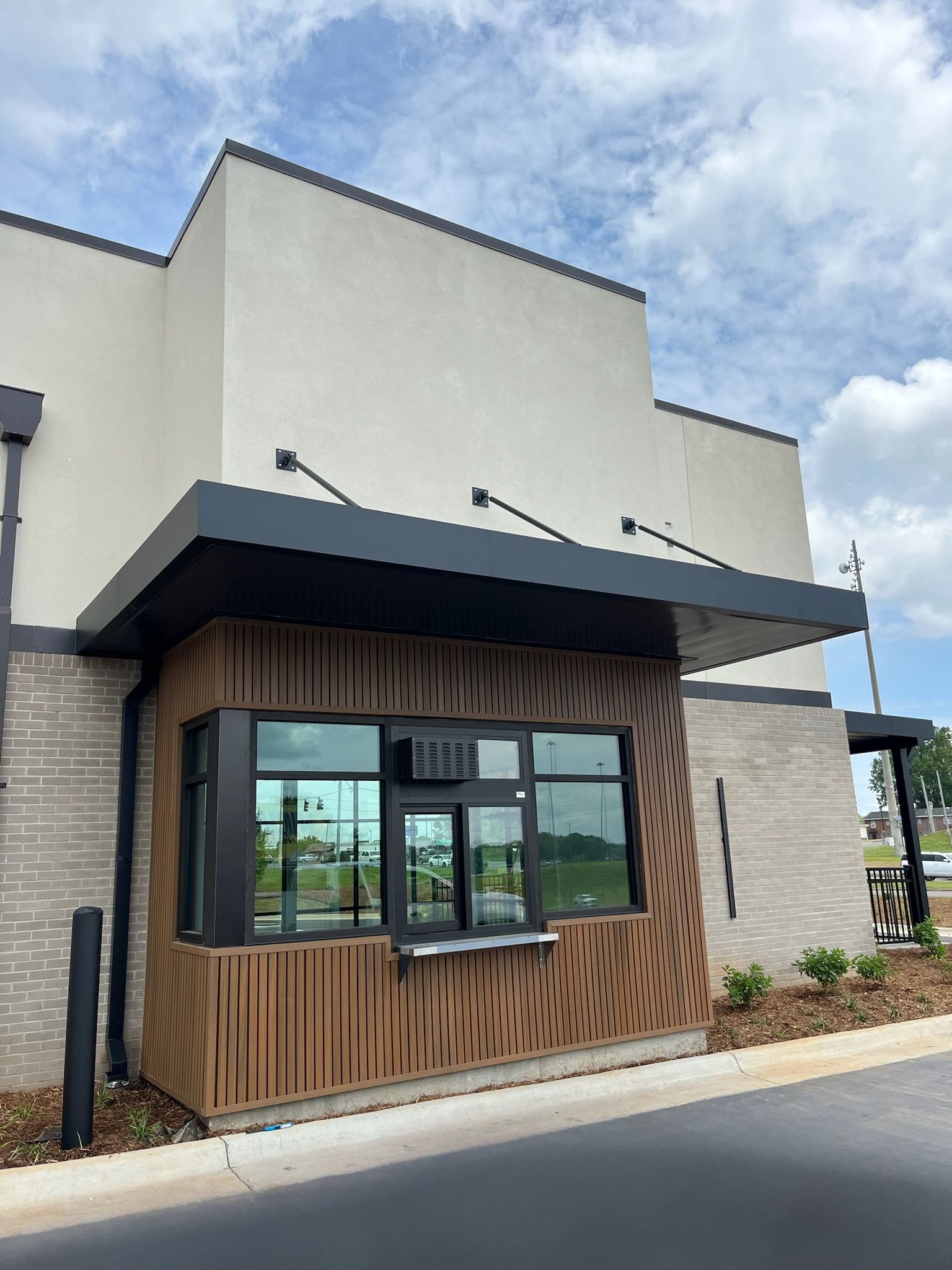 Drive-through window with brown wood-grain paneling. Gray and tan building exterior, black awning, blue sky.