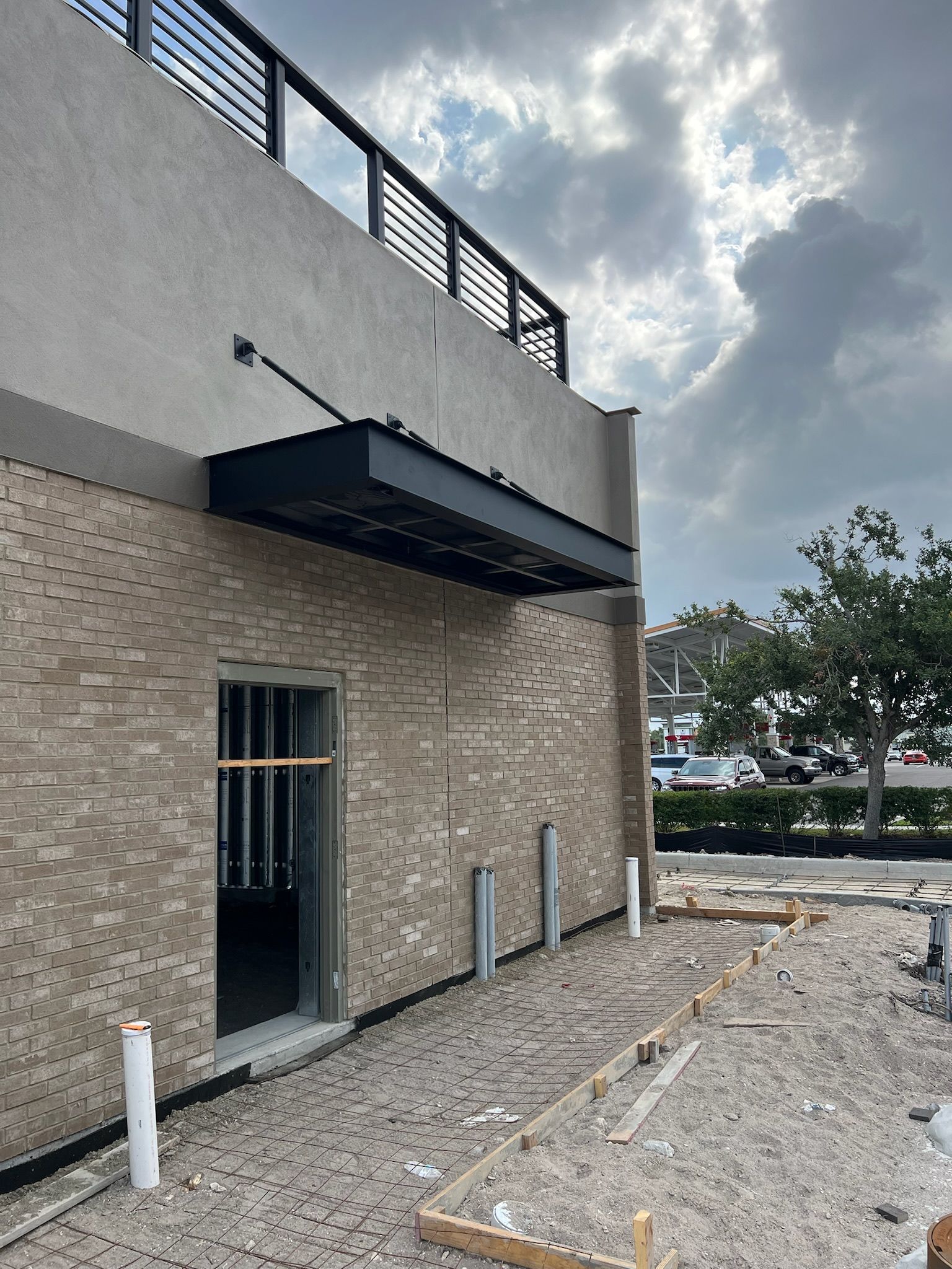Exterior of a building under construction, with brick facade, metal awning, and cloudy sky.