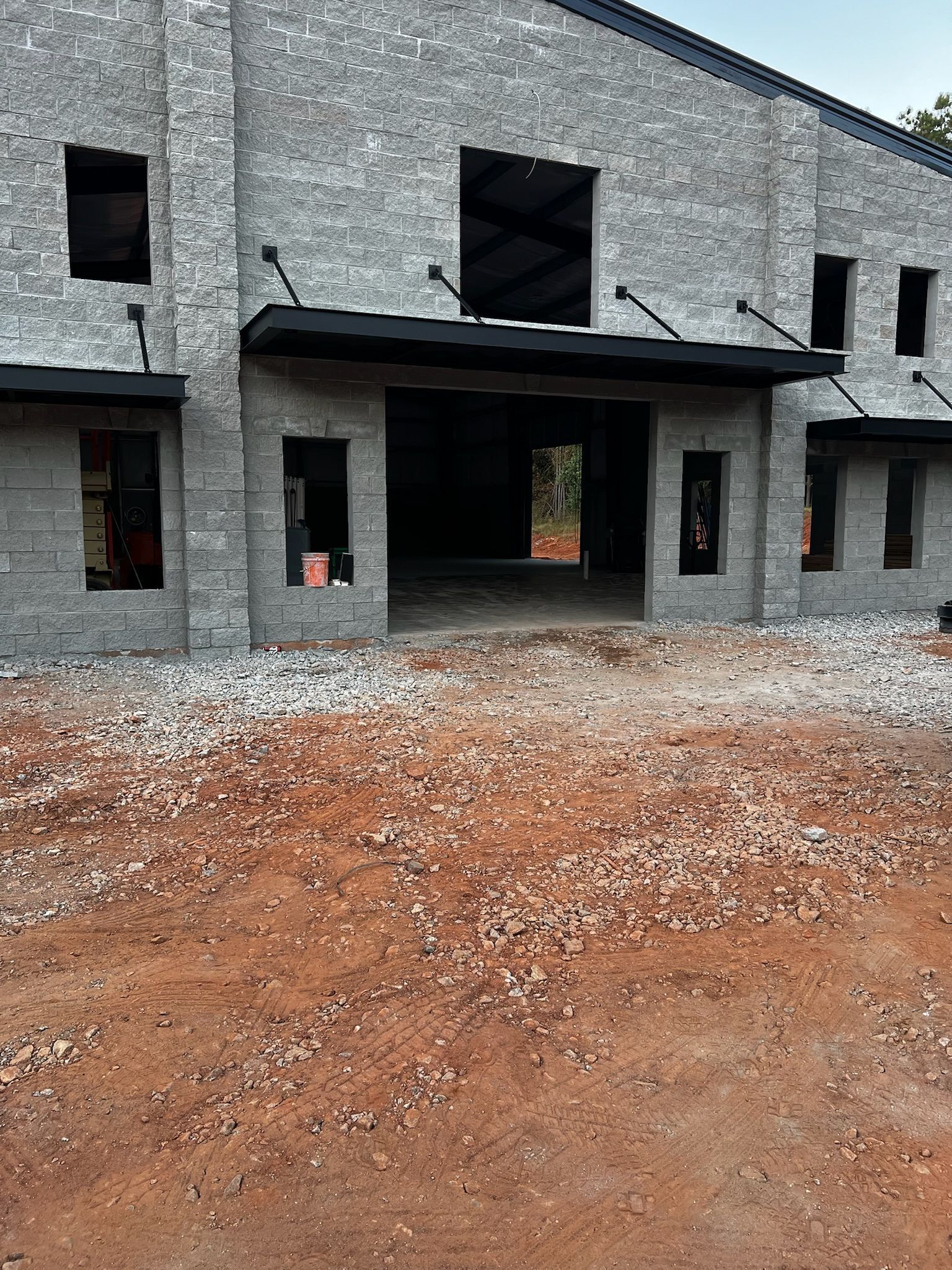 Brick building exterior under construction, dirt and gravel foreground, black awning.