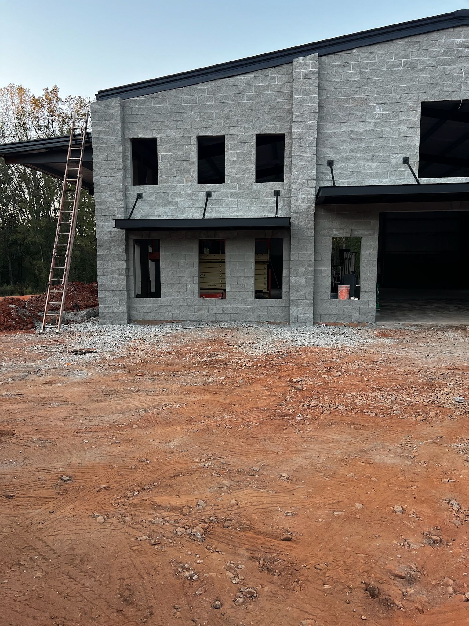 Building under construction with gray brick exterior, bare window frames, and surrounding dirt.