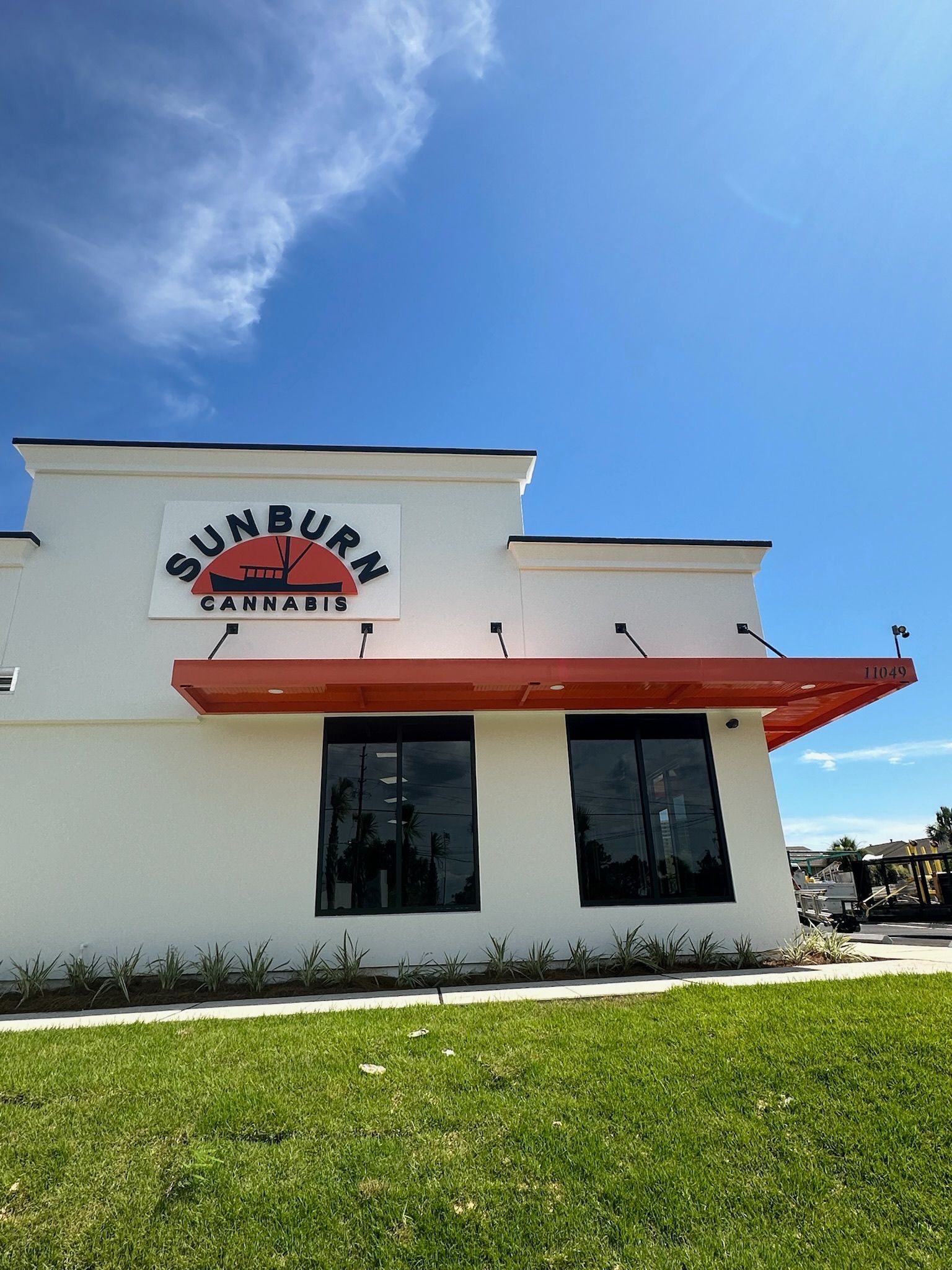 Sunburn Cannabis storefront with orange awning, white building, and blue sky.