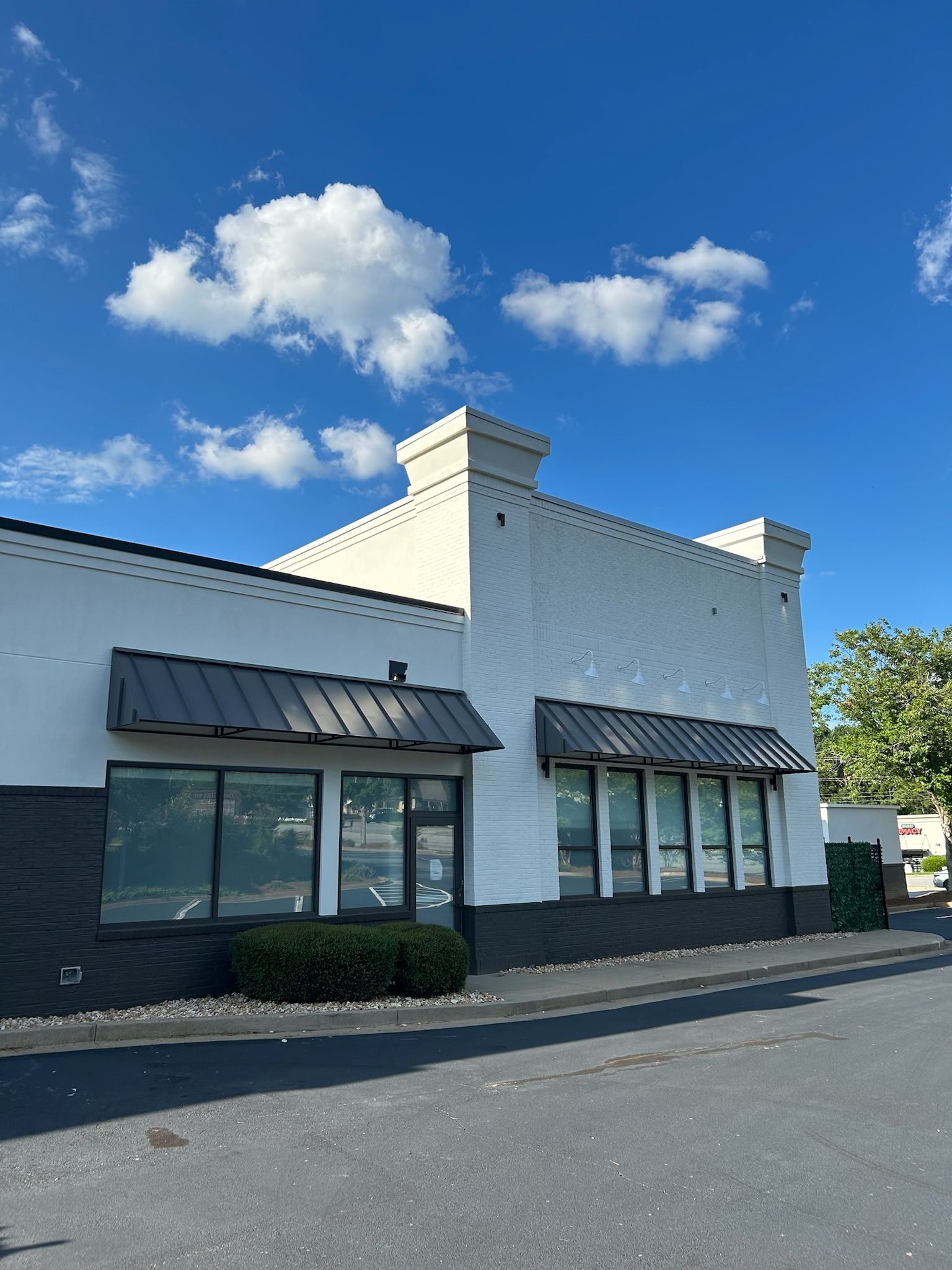 White brick building with dark awnings, windows, and black trim against a blue sky with clouds.