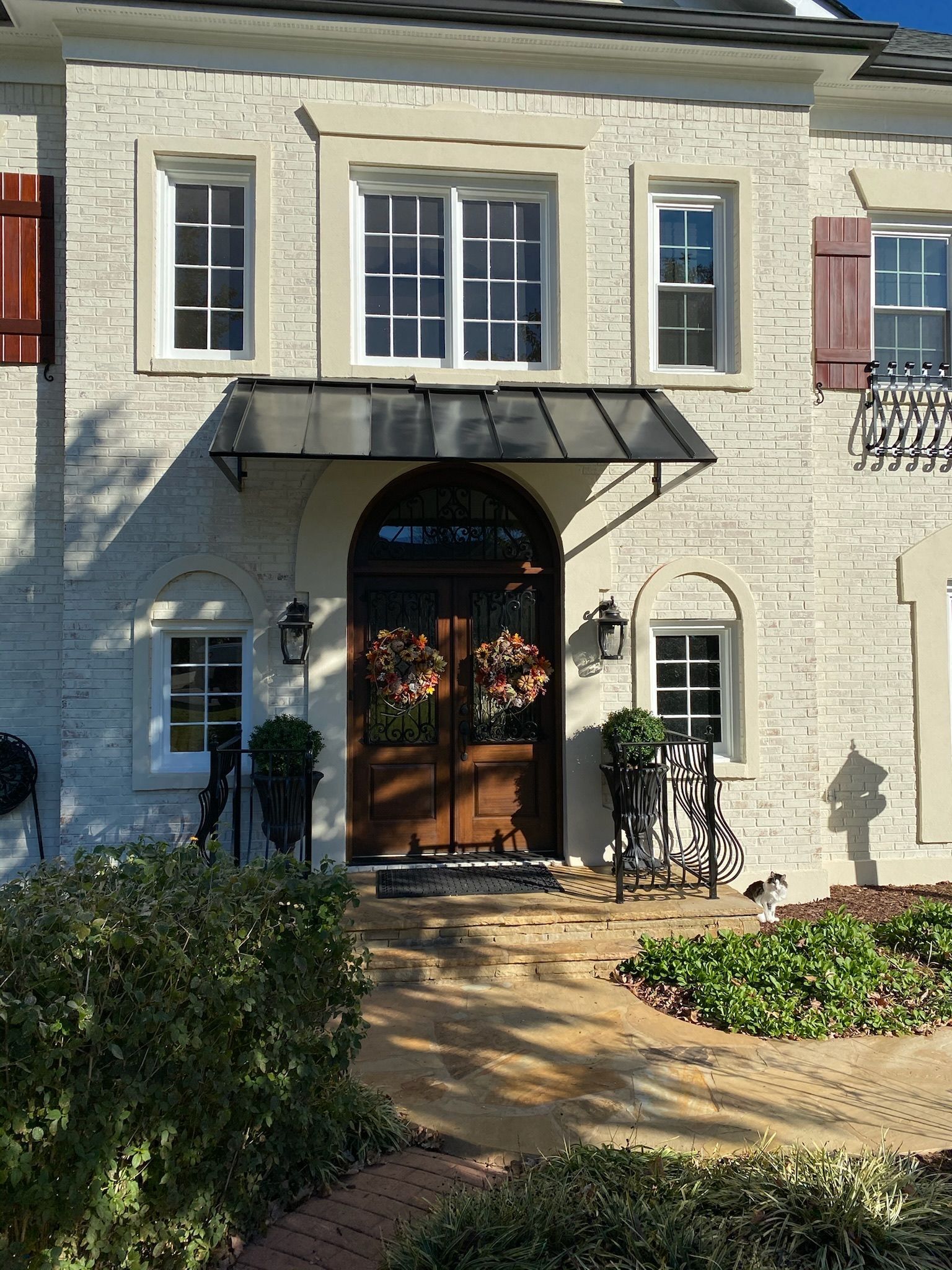 A brick house with a dark metal awning over the front door, flanked by windows and shutters.