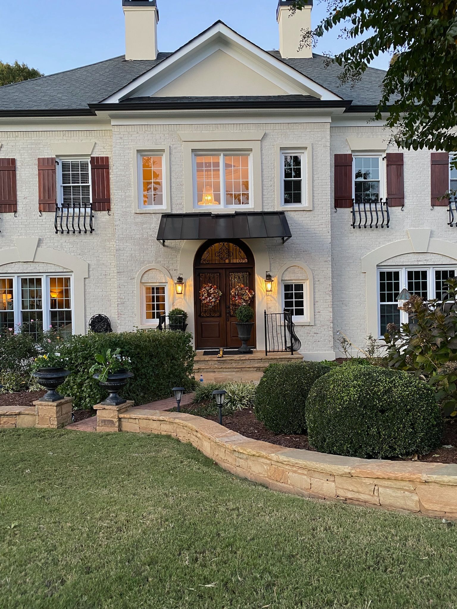 White brick house with dark shutters, arched entryway, and lit interior.