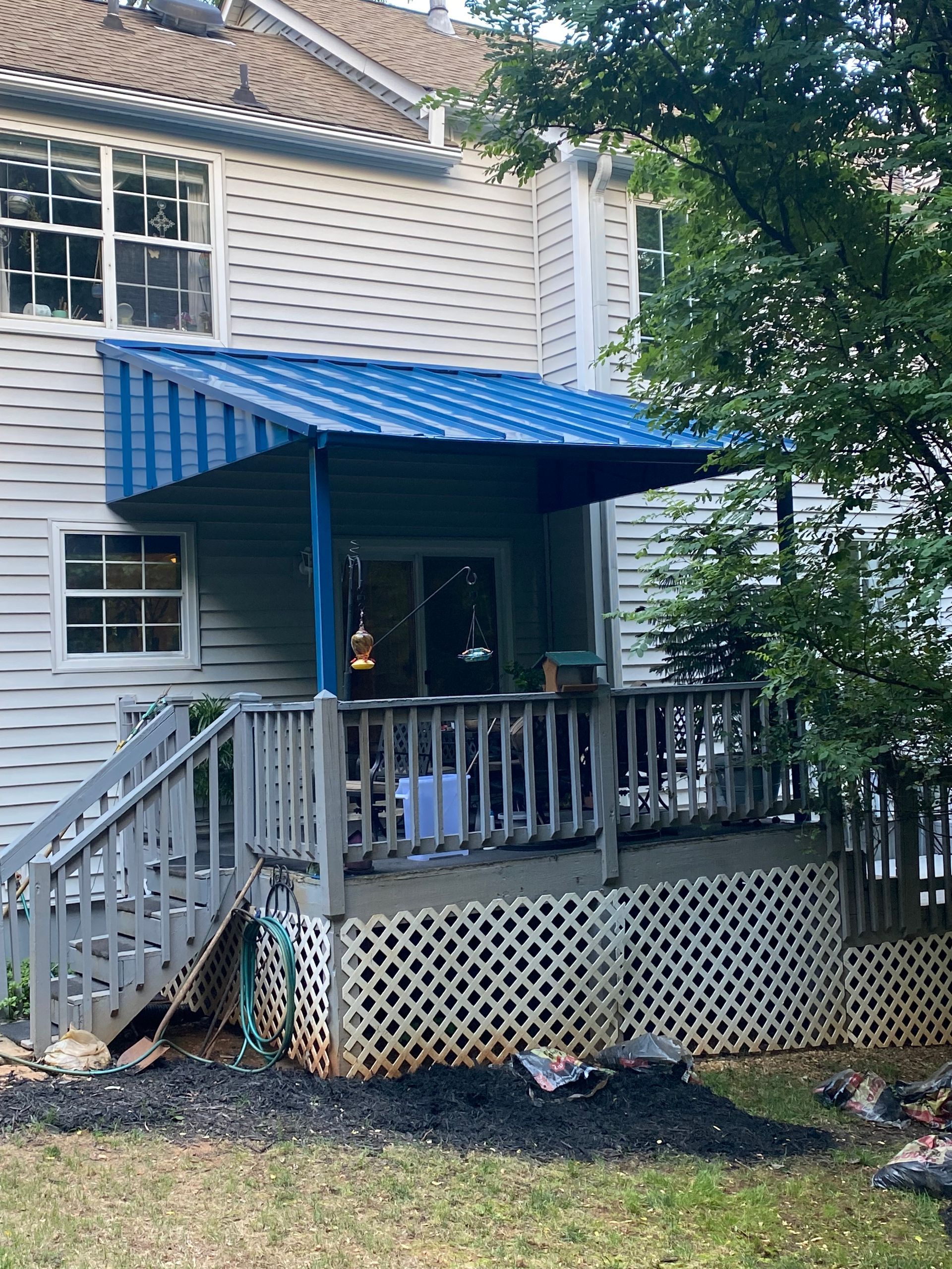 Blue metal awning over a wooden deck with white siding and a staircase.