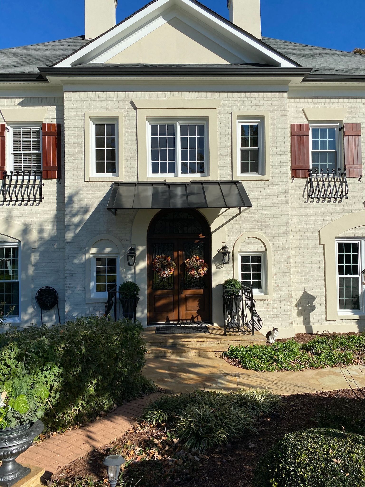 Two-story brick house with a dark wood door, brown shutters, and landscaping.