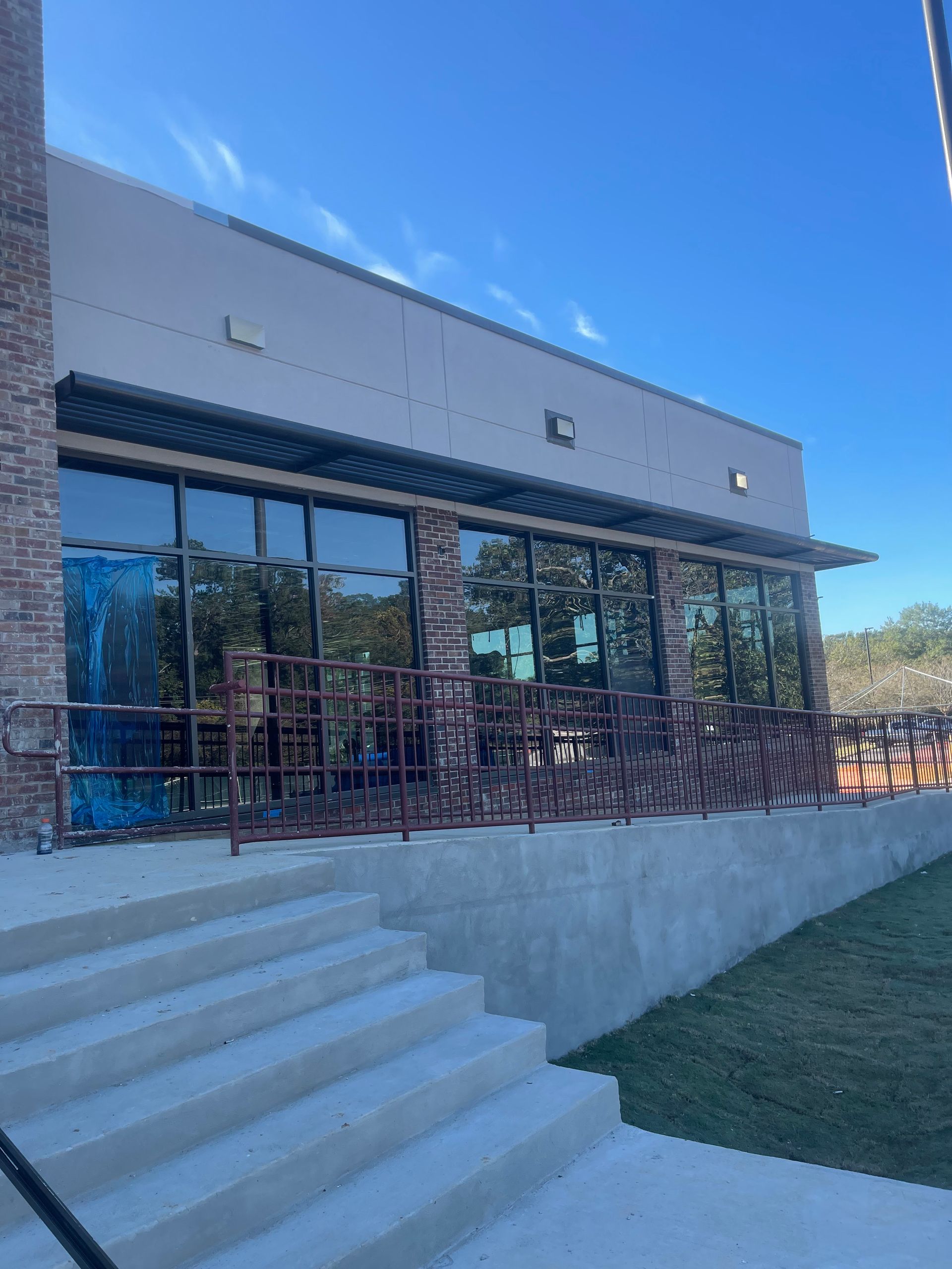 Building with brick and glass facade, outdoor seating, concrete steps, and blue sky.