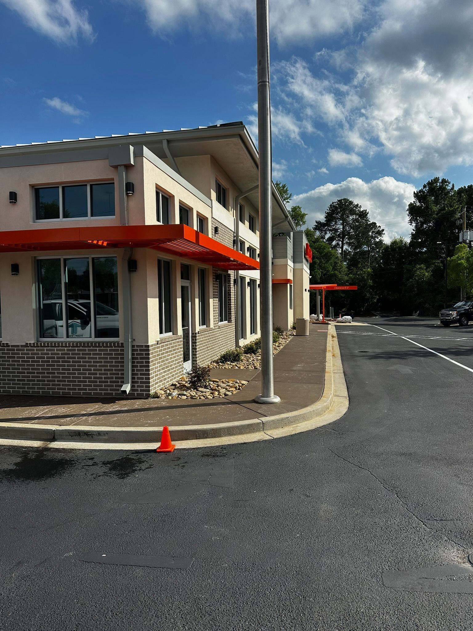 Exterior of a modern building with red accents, set against a blue sky with clouds. A paved road curves around.