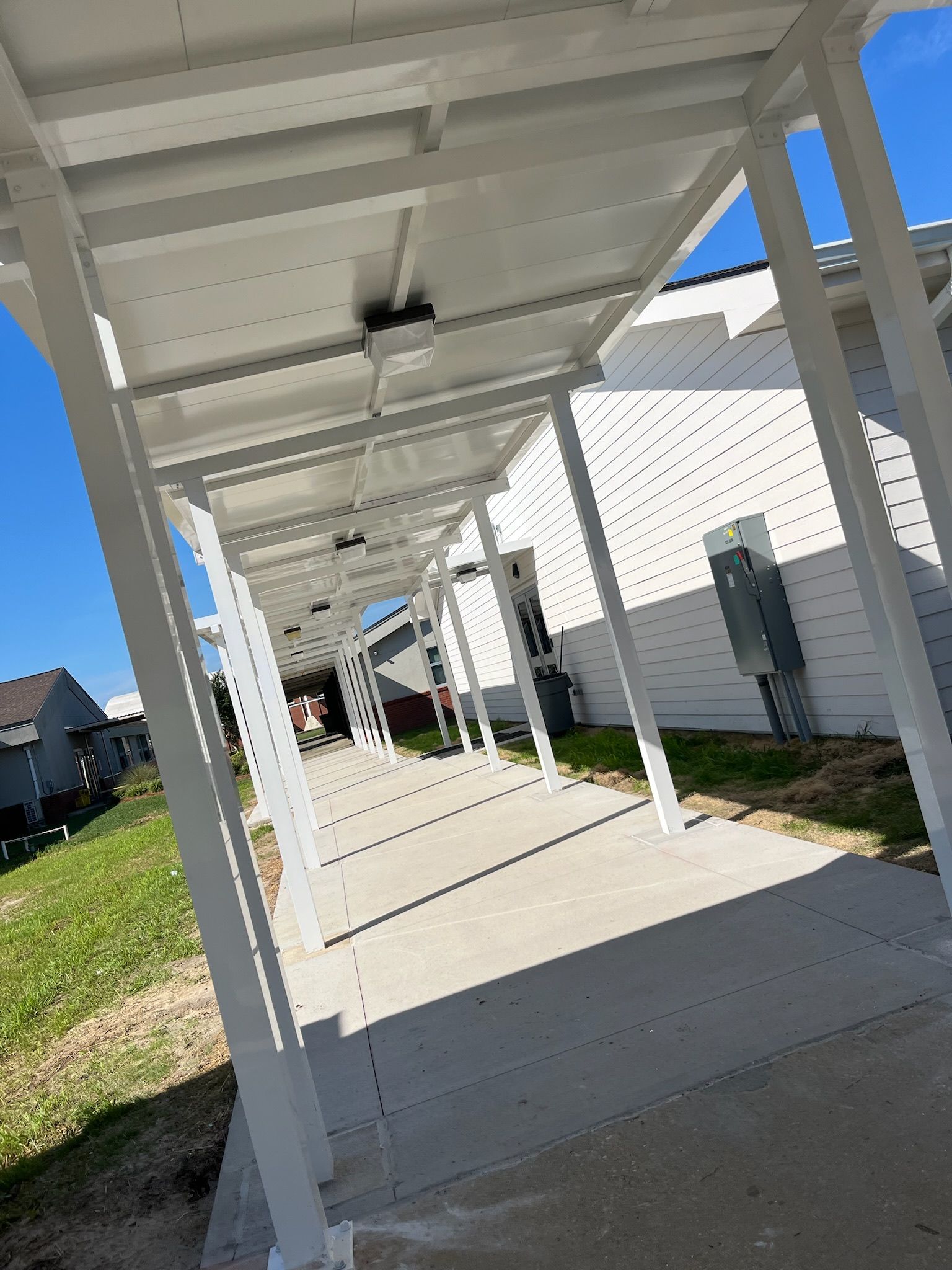 White covered walkway with concrete path, grass, and a blue sky.