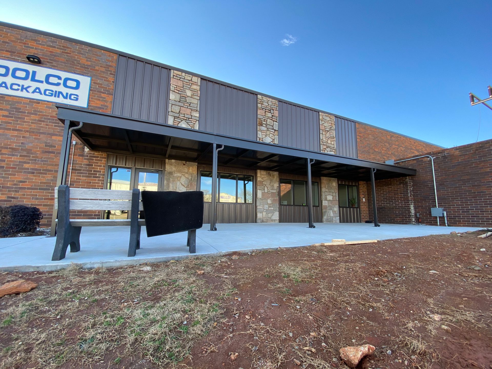 Building exterior with a covered entrance, bench, and stone accents. 