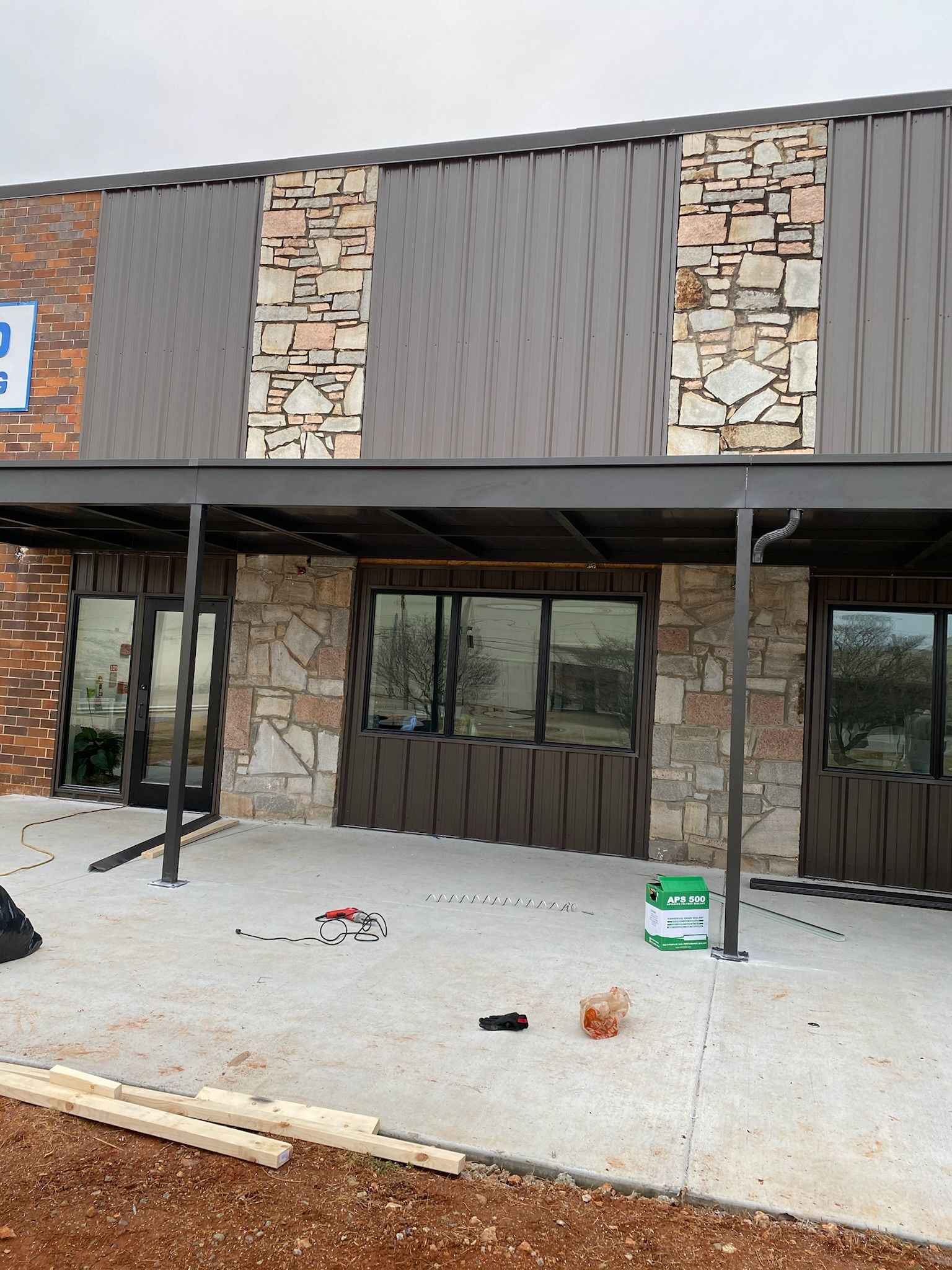 Building exterior with metal roof, stone and brick facade, and covered entrance under construction.