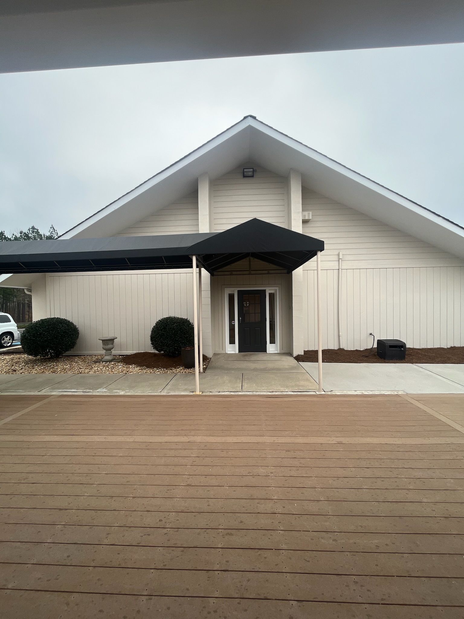 White church building with black awning over the entrance. Gray sky, brown driveway.