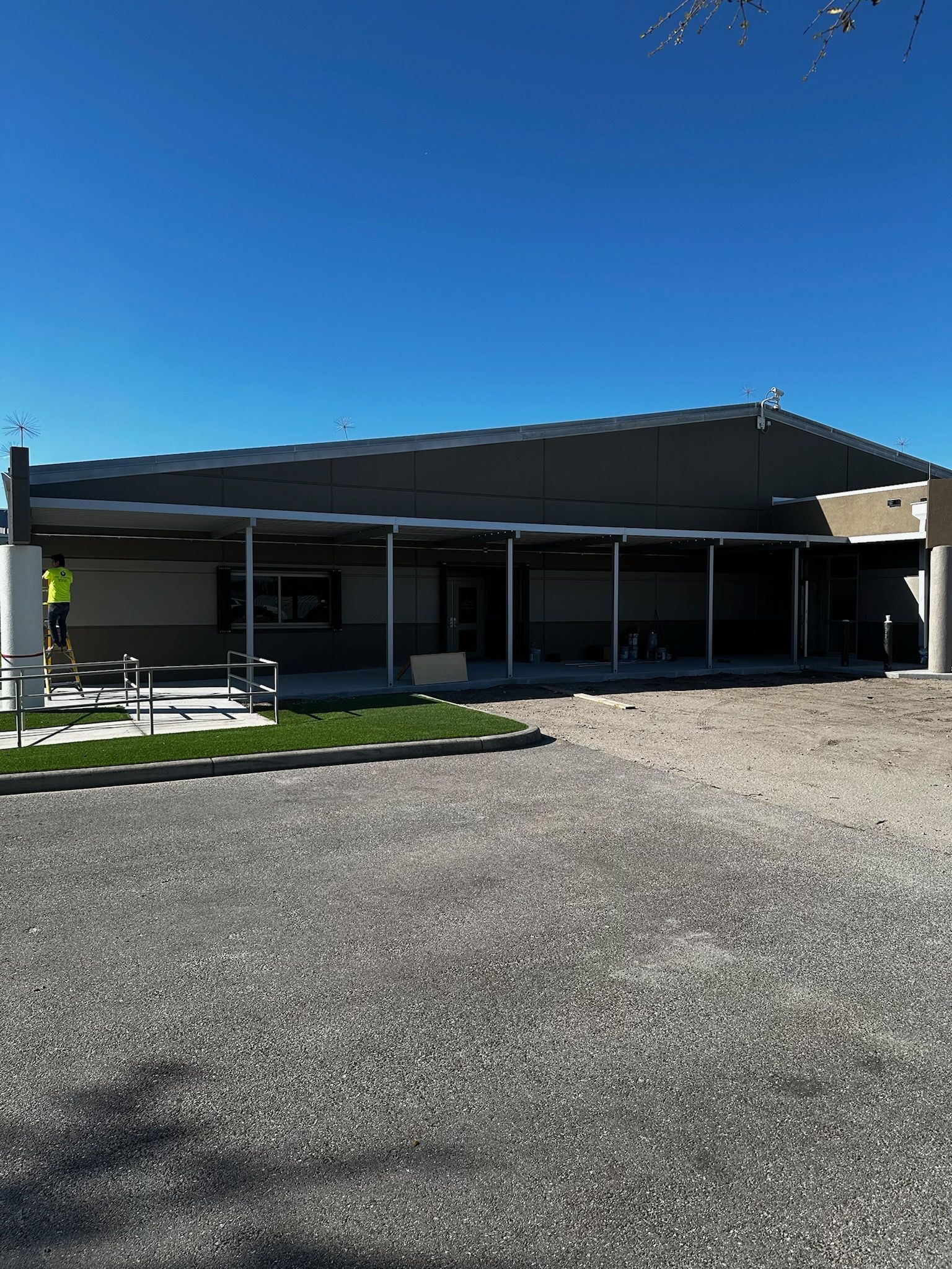 Building with long covered patio, gravel area in foreground, blue sky.