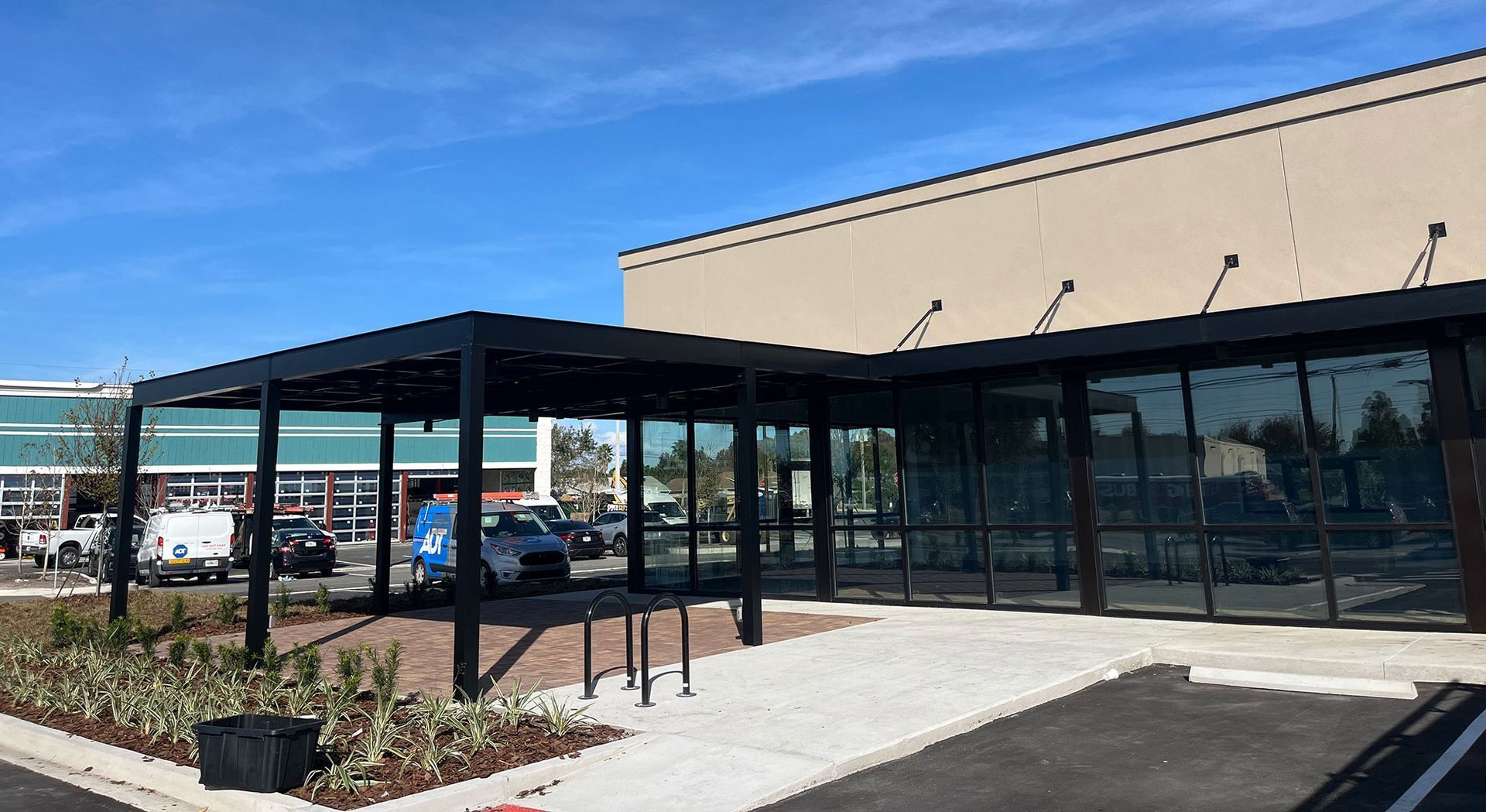 Exterior of a modern building with a black pergola over an entrance, clear glass windows, and a blue sky.