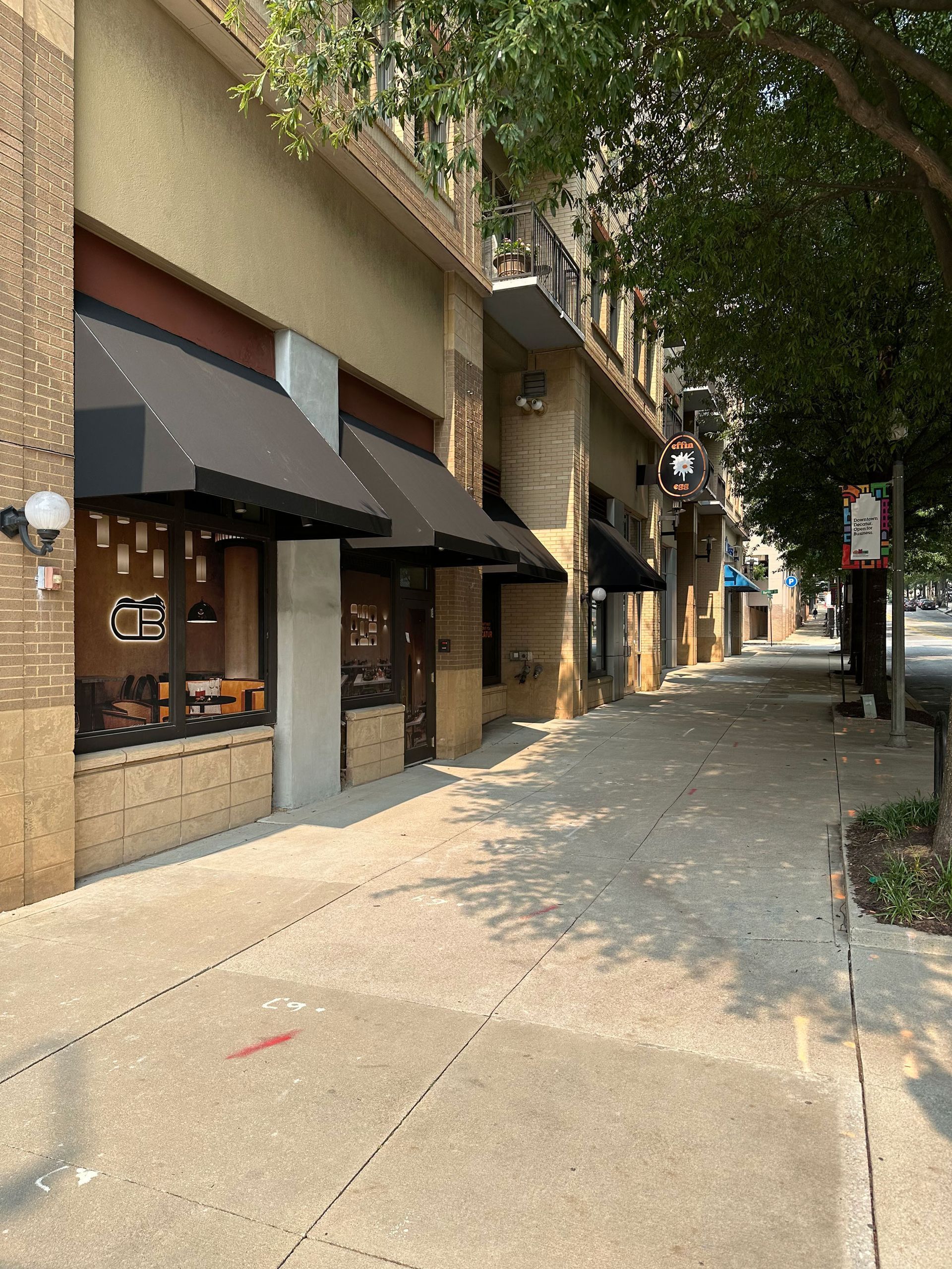 Sidewalk next to buildings with awnings, one storefront visible with a sign.