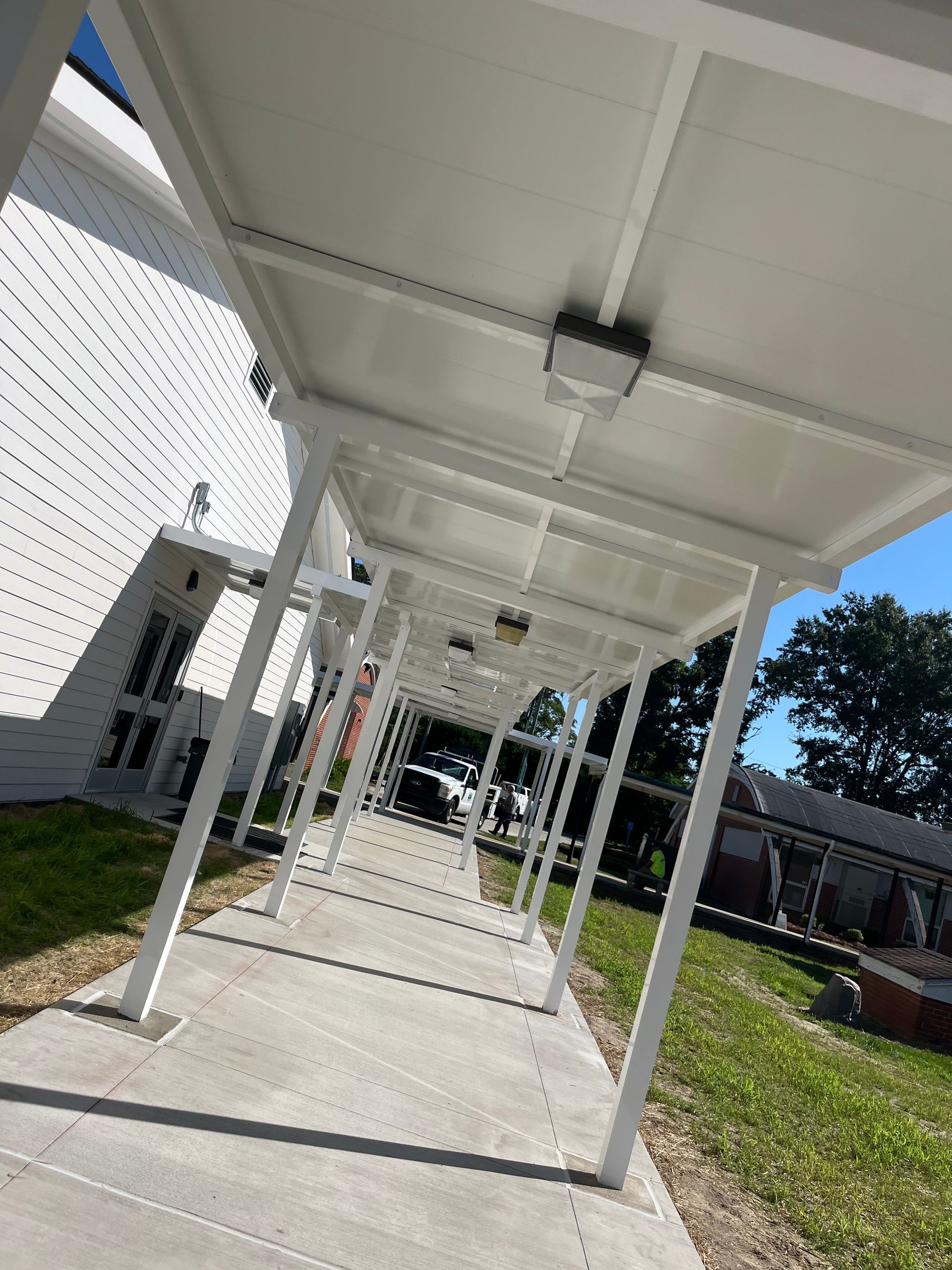 White covered walkway along a building's exterior. Concrete path with a blue sky visible ahead.