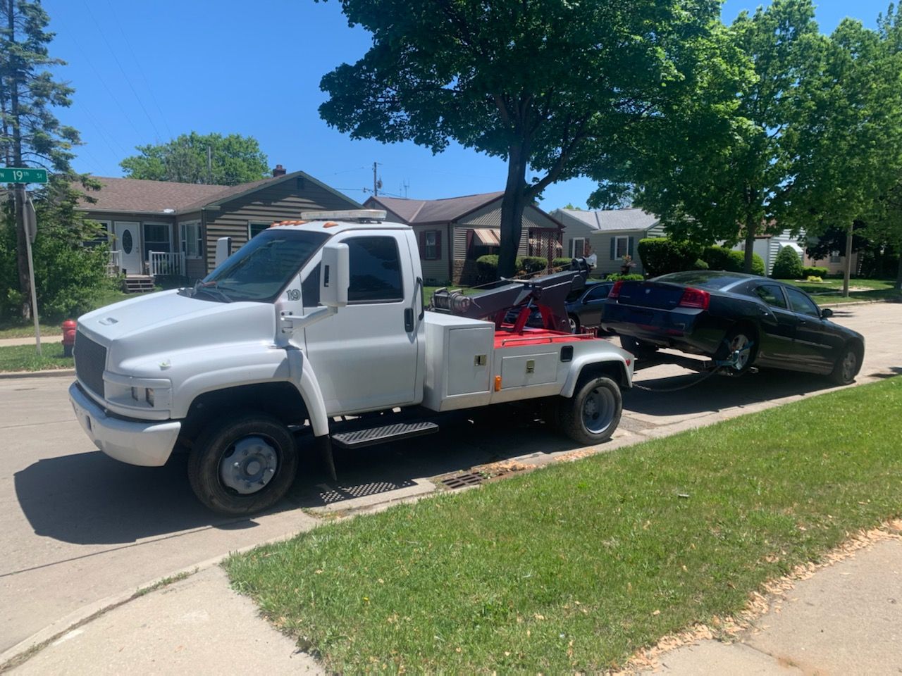 A white tow truck is towing a black car down a street.