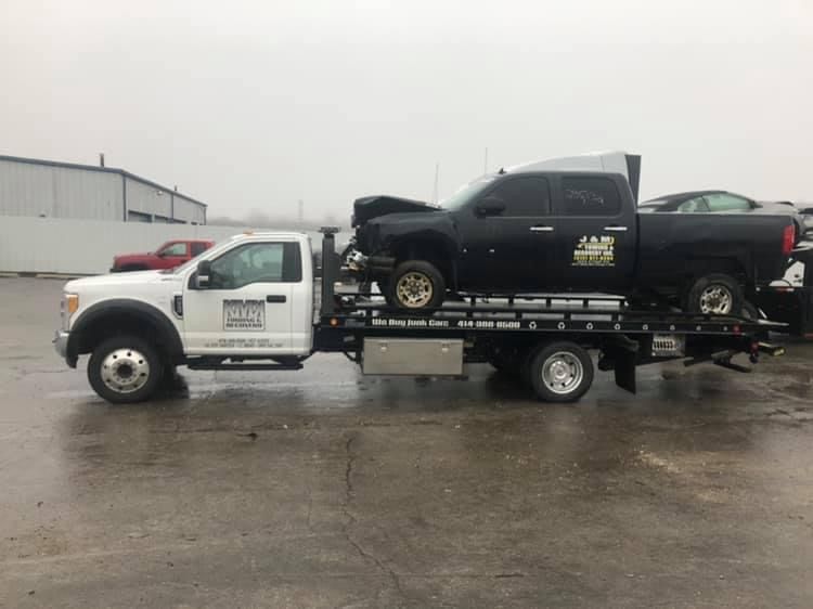 A tow truck is carrying a black truck and a white truck.