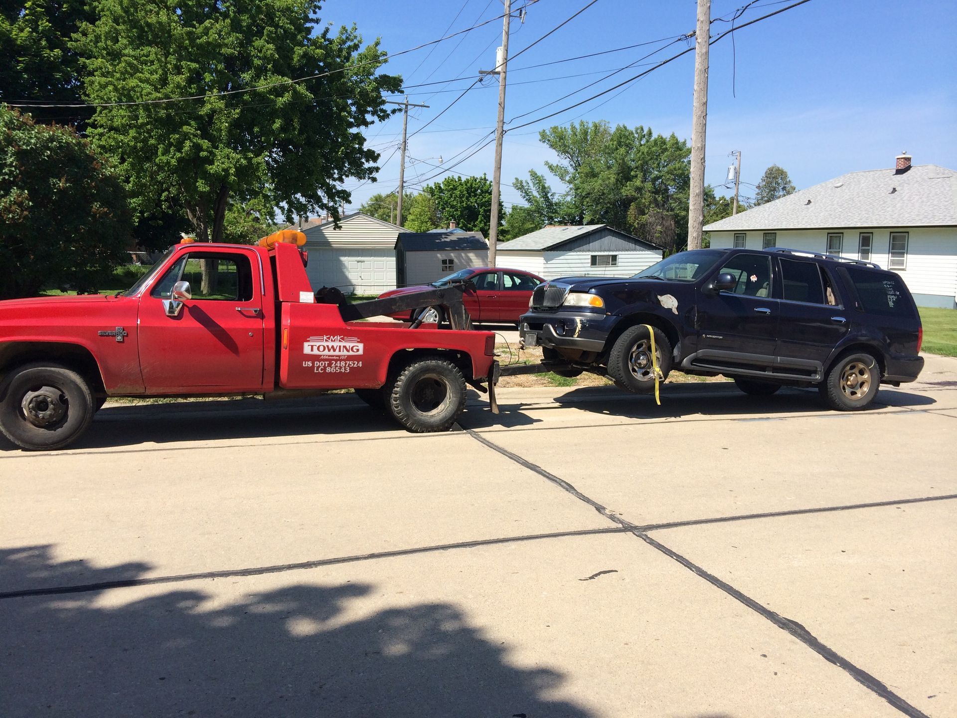 A red tow truck is towing a black suv on a street.