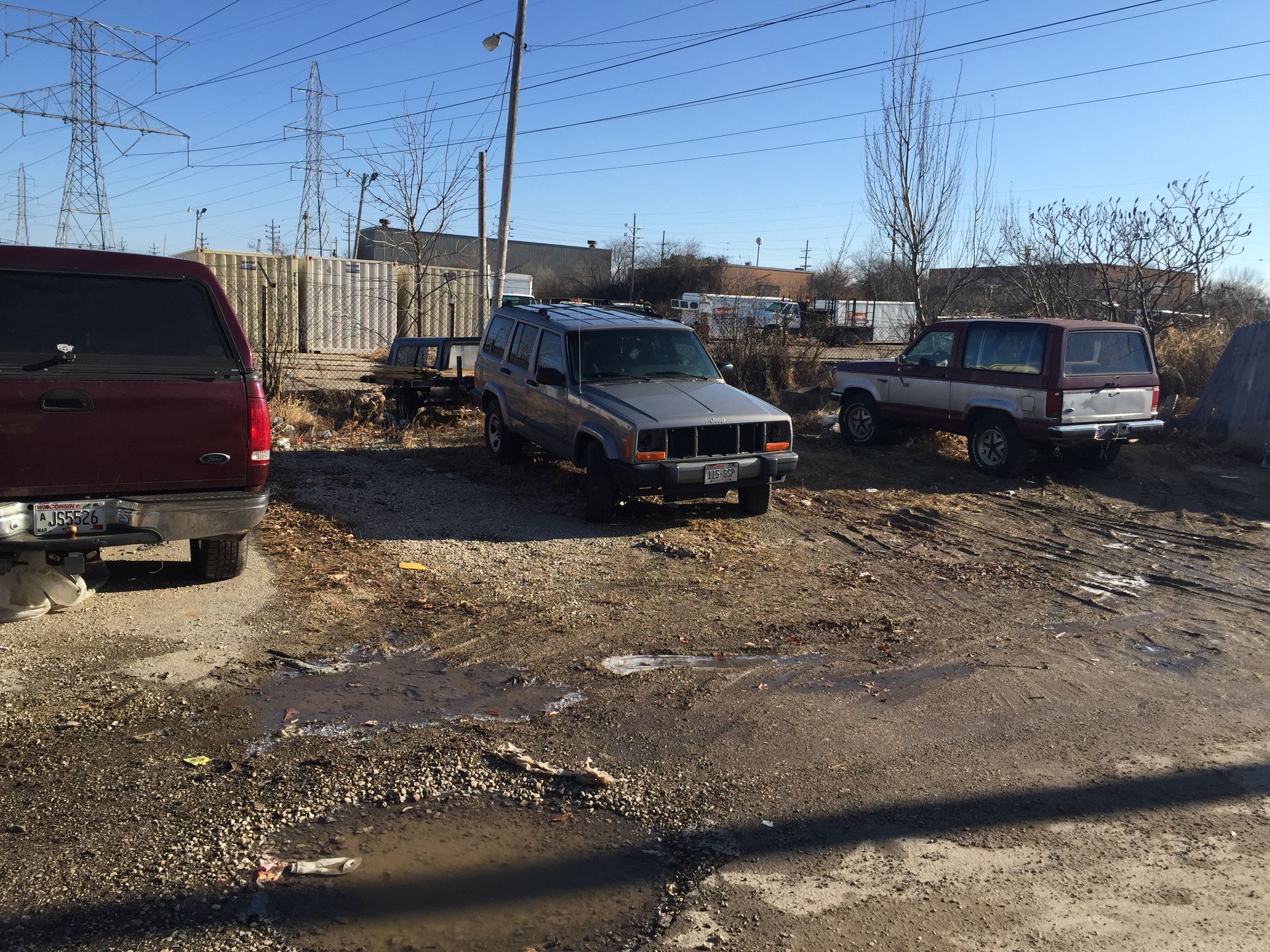 A red truck is parked next to a silver suv in a dirt lot.