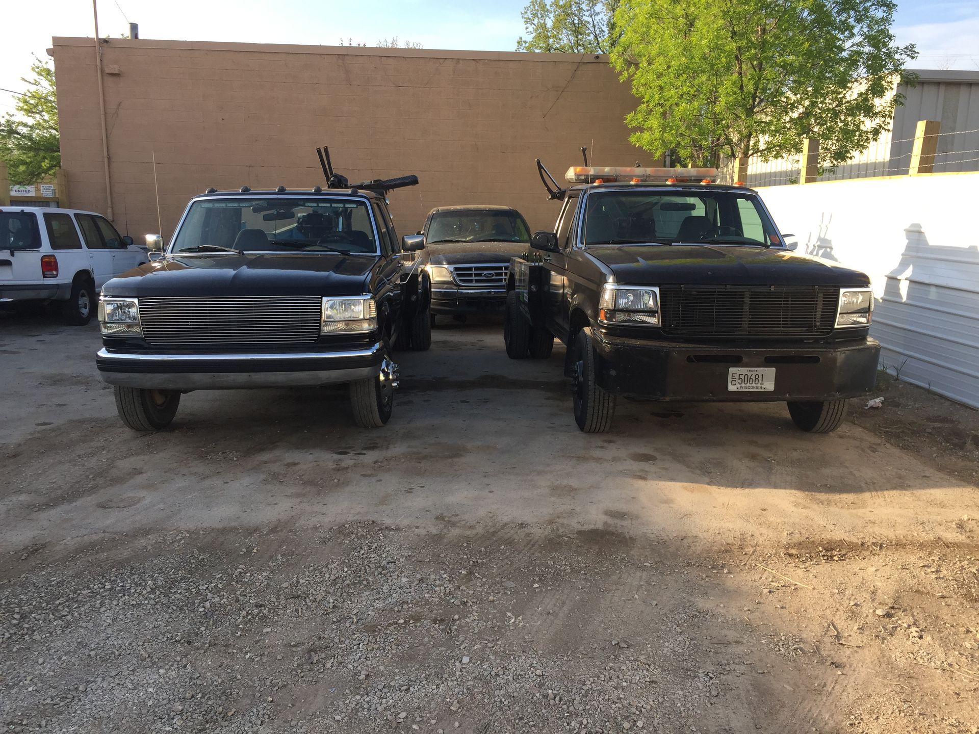 Three trucks are parked in a gravel lot in front of a building.