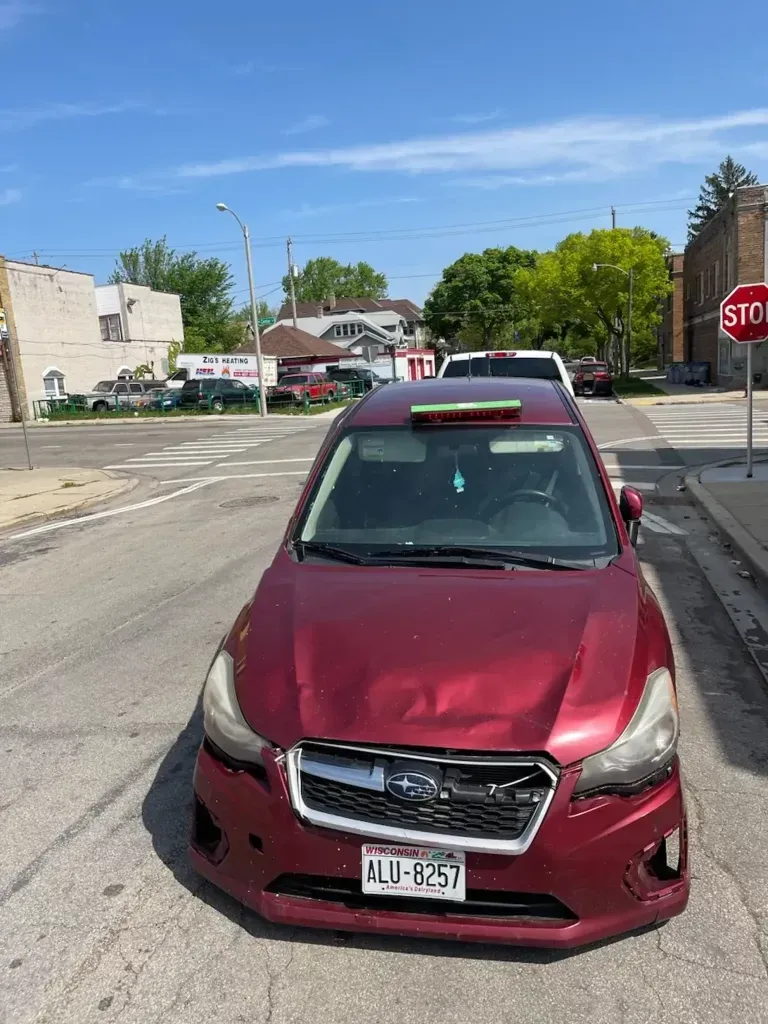 A red car is parked on the side of the road next to a stop sign.