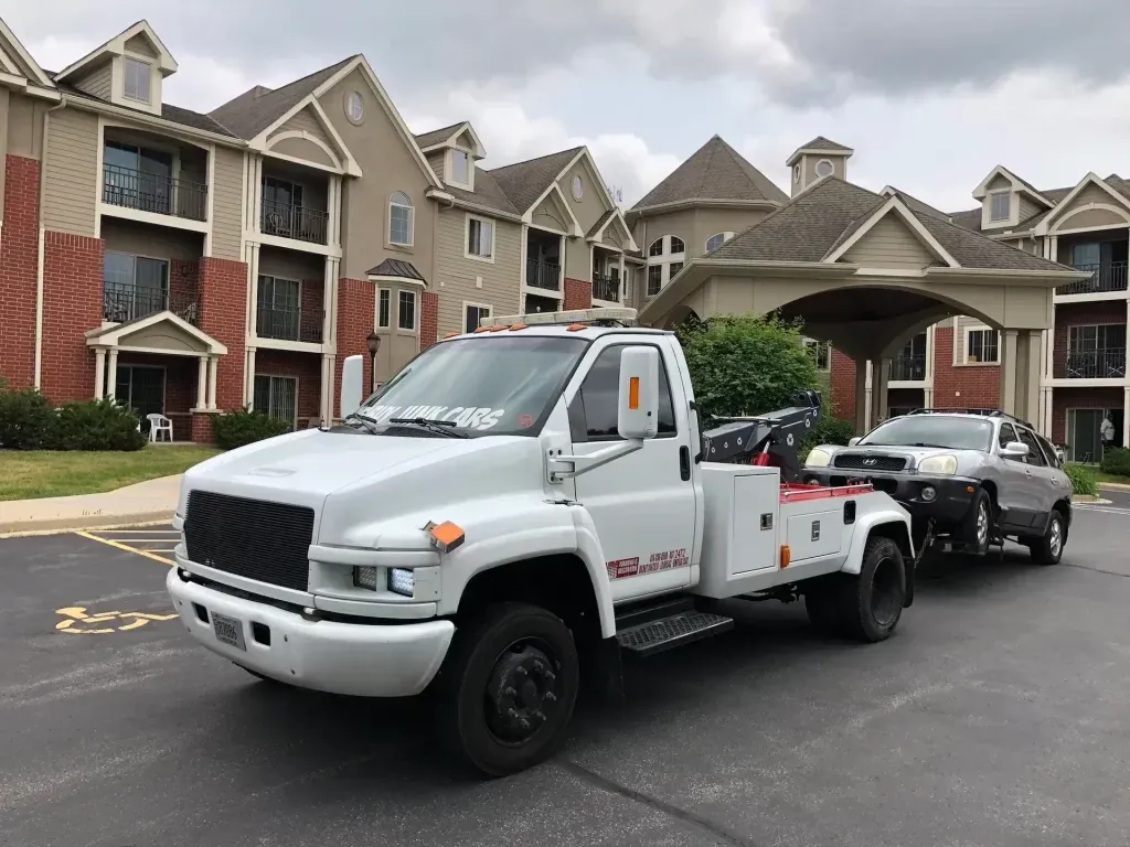 A white tow truck is towing a car in front of a building.