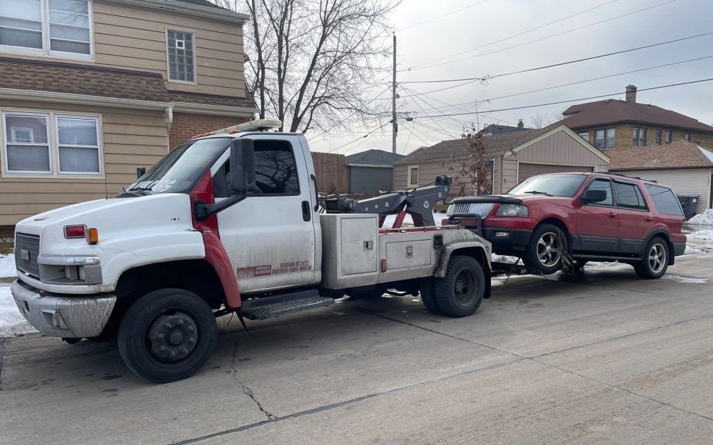A white tow truck is towing a red suv down a street.