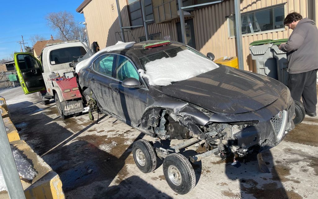 A man is standing next to a damaged car on wheels.