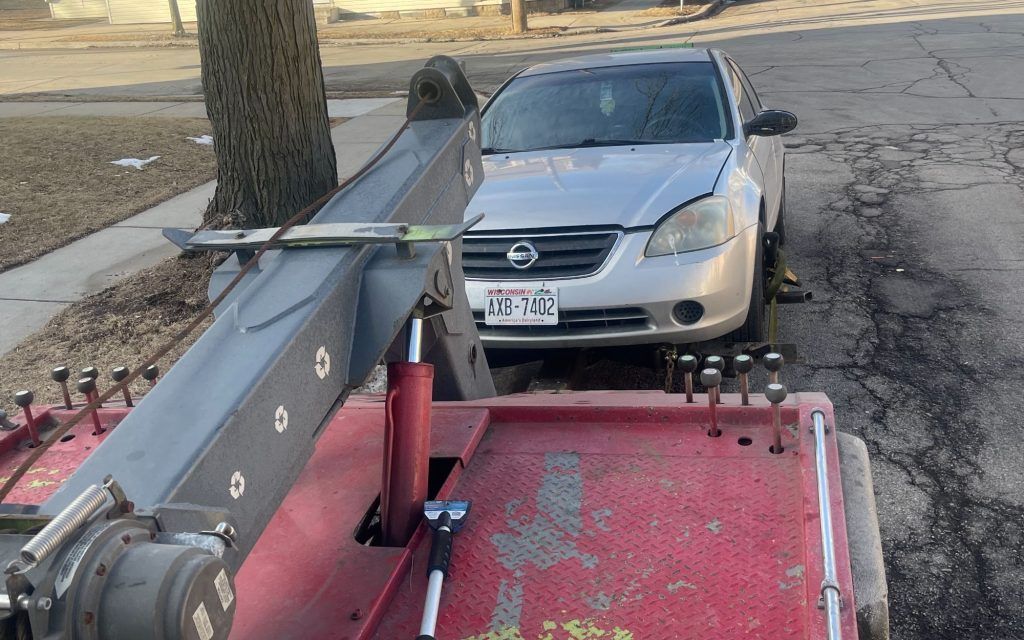 A silver car is being towed by a tow truck