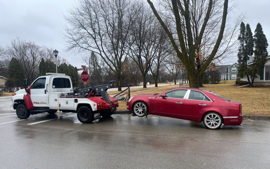 A tow truck is towing a red car in a parking lot.