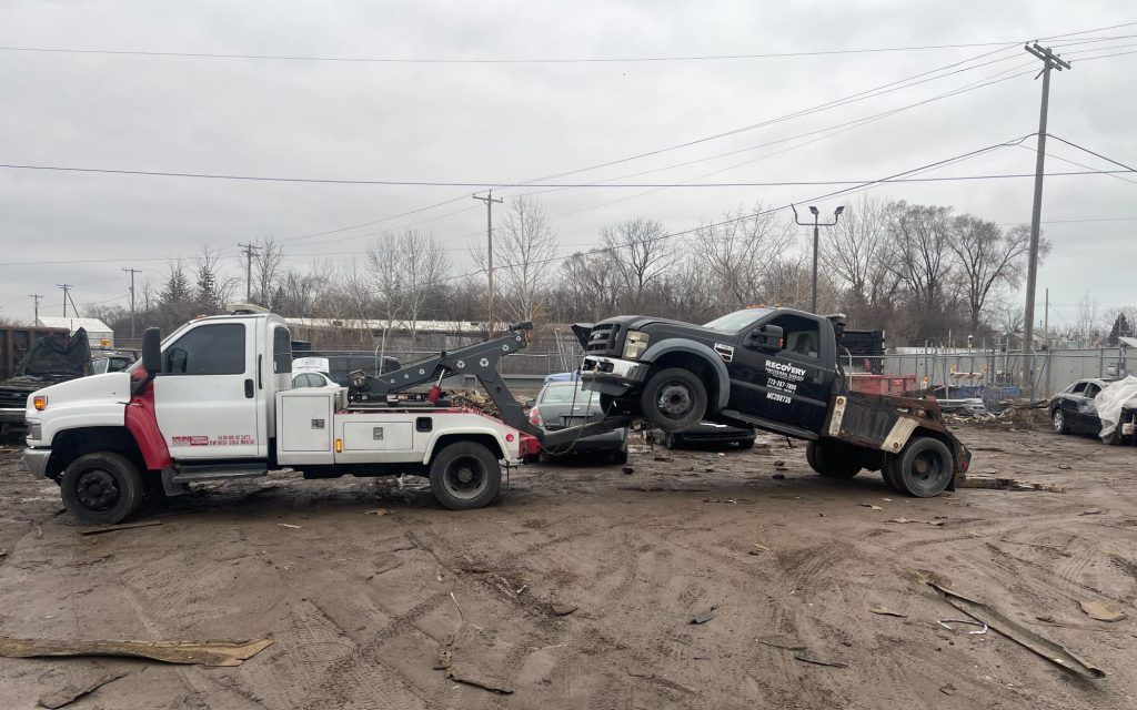 A tow truck is towing a car in a muddy field.