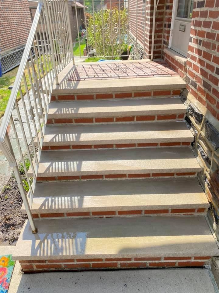 Concrete steps with brick trim leading to a brick building's entrance. Metal railing on the left.
