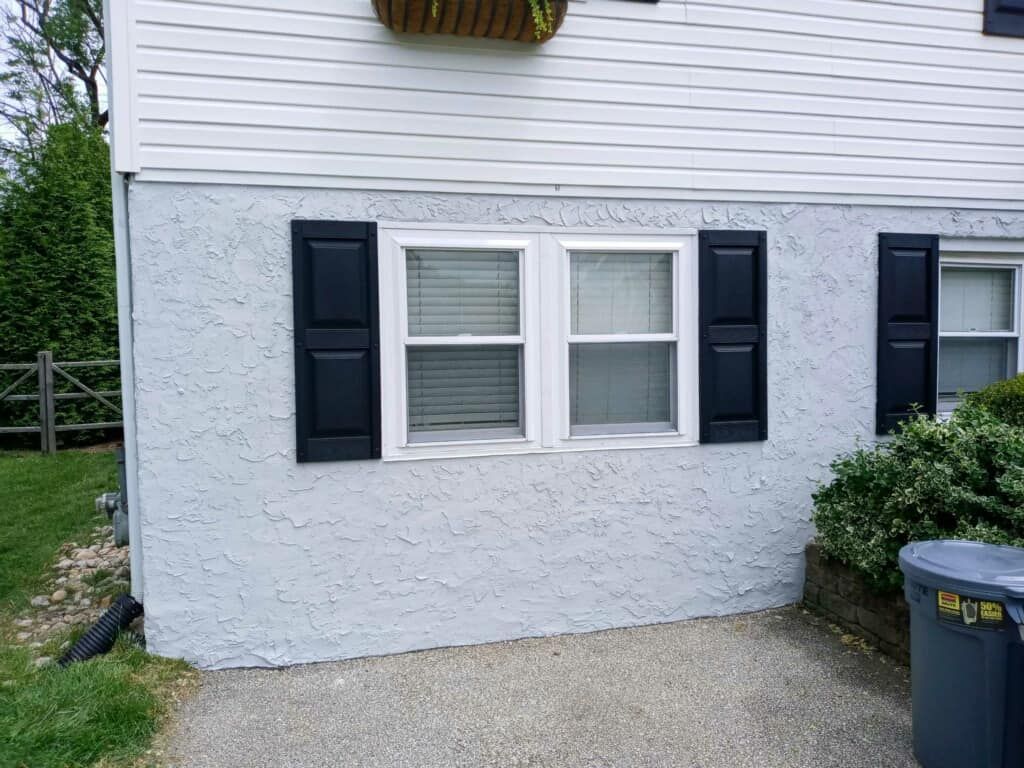 House exterior with blue shutters, two windows, and textured blue stucco siding.