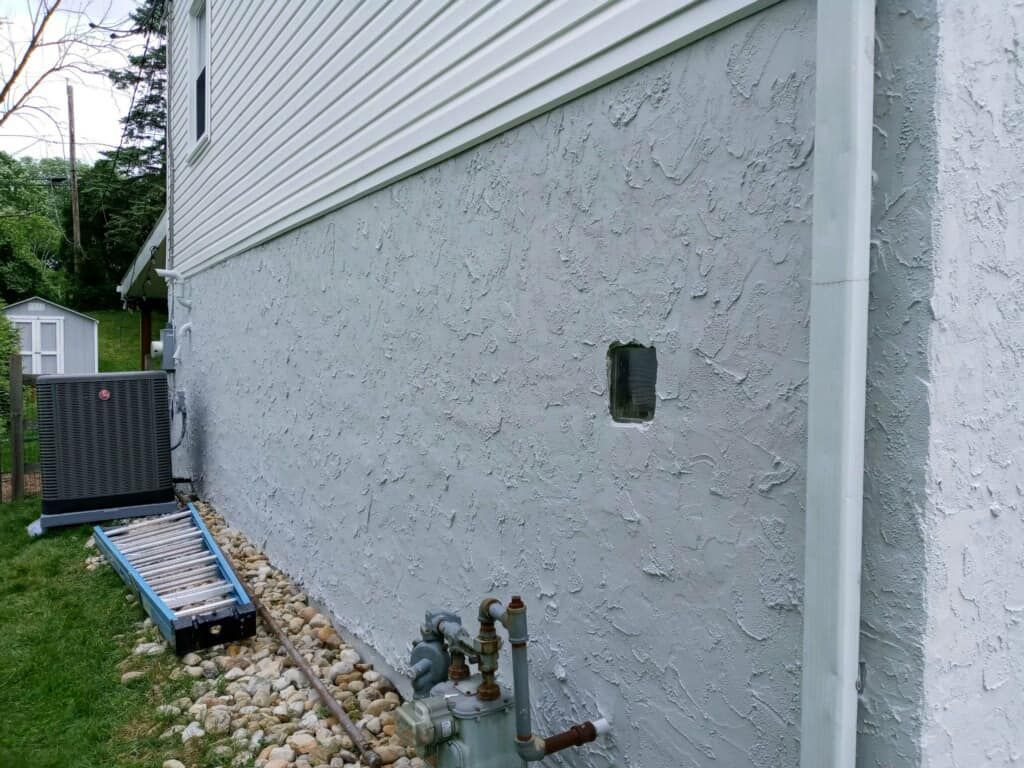 Exterior house wall with textured grey stucco, utility box, and gas meter.