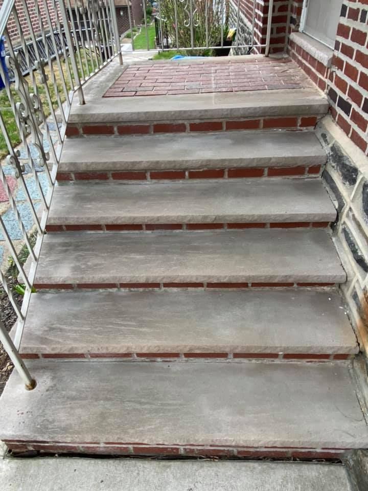 Concrete steps with brick trim leading to a porch with metal railing.