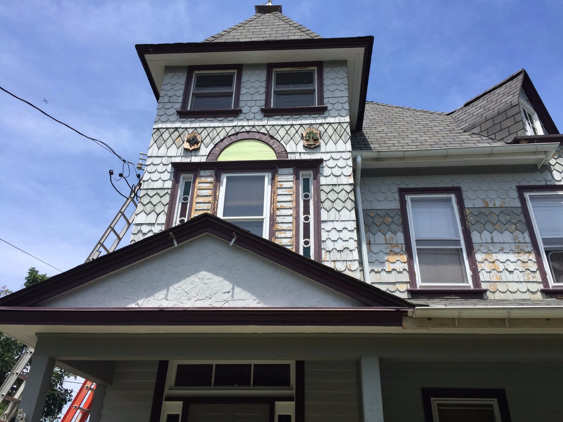 Victorian-style house with blue siding, brown trim, and a prominent tower under a blue sky.
