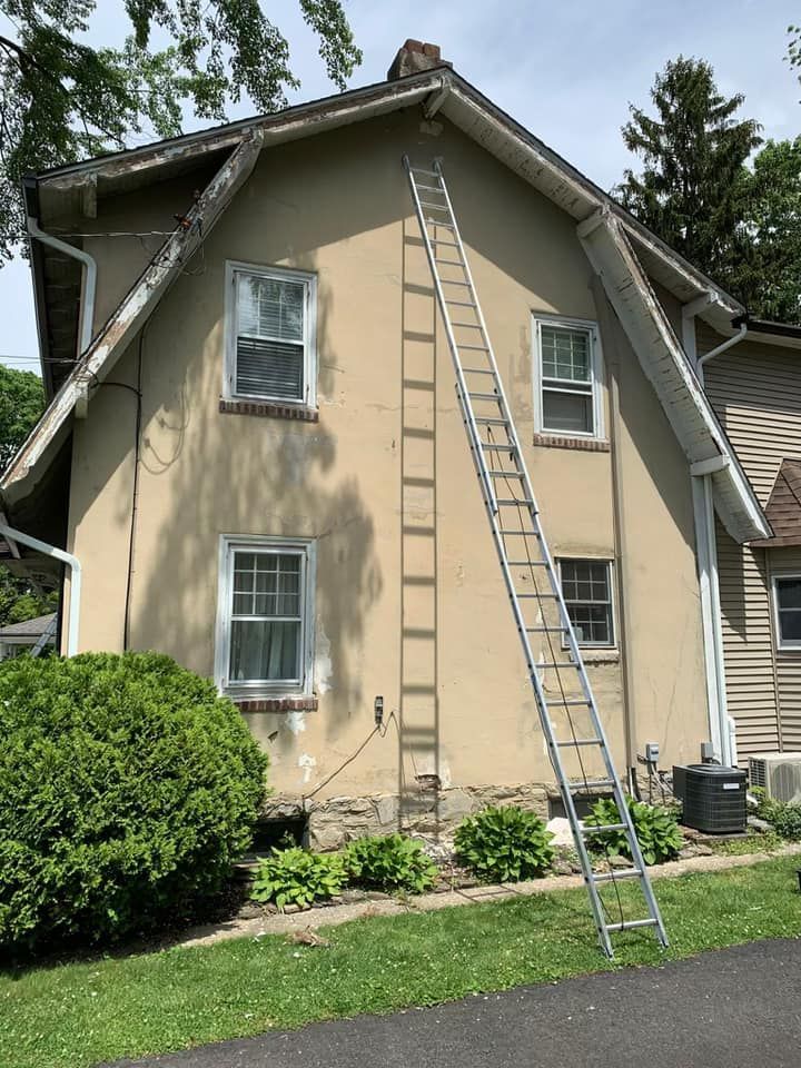 A tall ladder leaning against a two-story beige house with a chimney.
