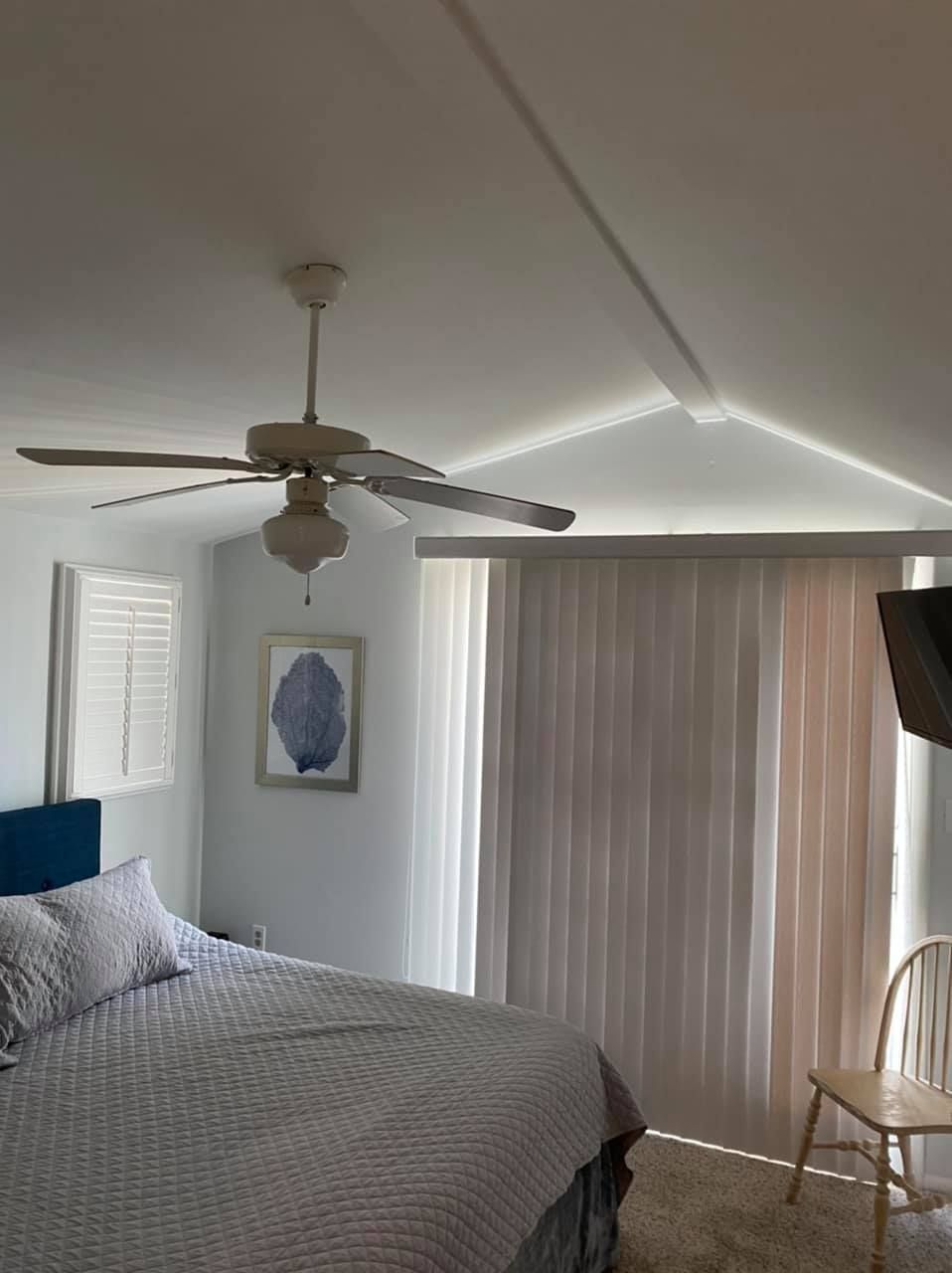 Bedroom with bed, ceiling fan, curtains, and wall art. Soft light.