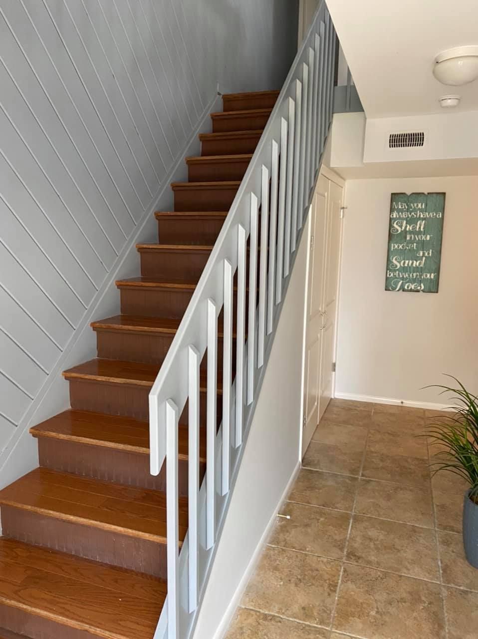 Wooden staircase with gray railing. The wall to the left has wood paneling. There is a decorative sign on the wall.
