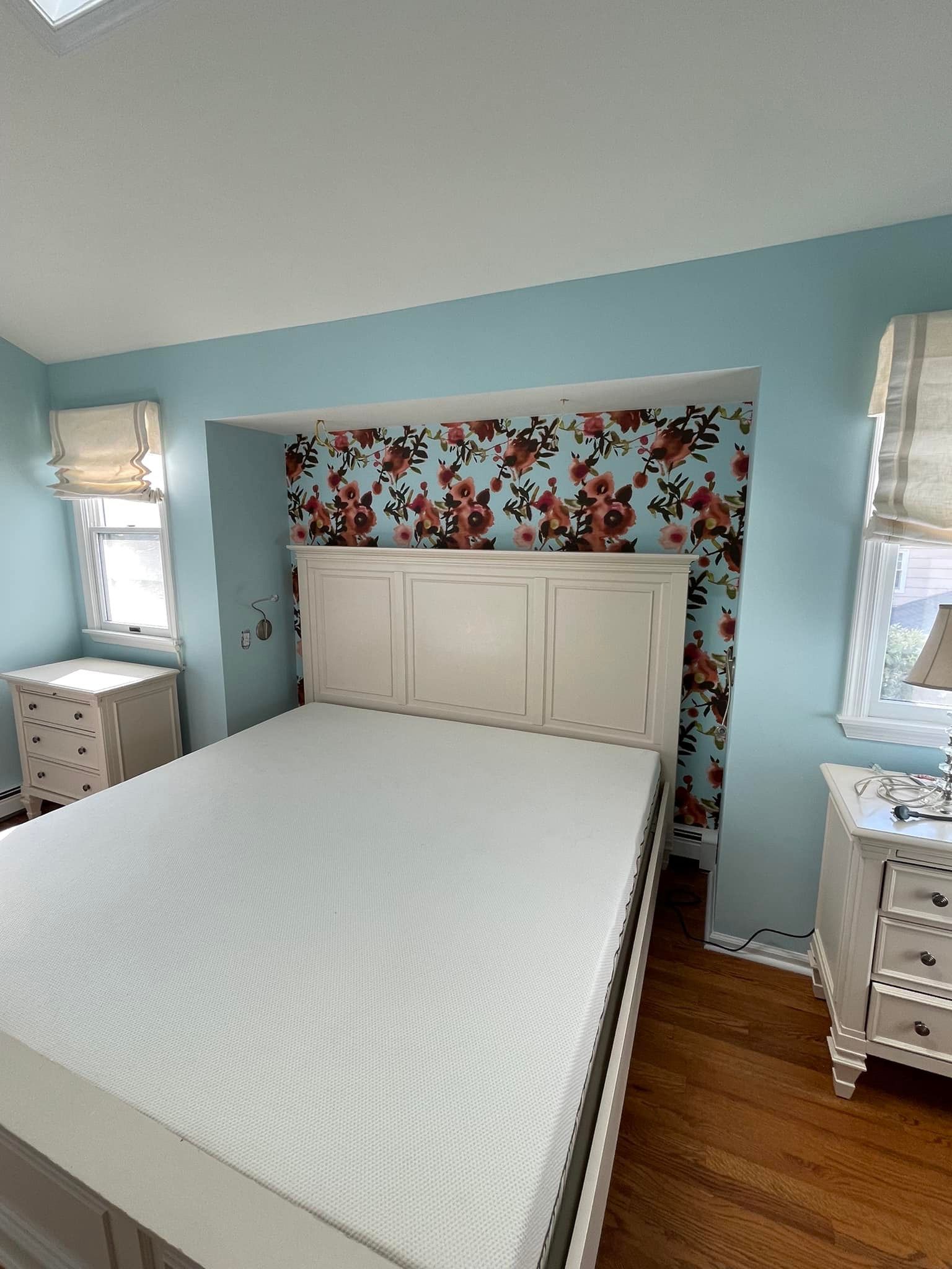 Bedroom with bed, white headboard, blue walls, floral wallpaper, and two bedside tables.