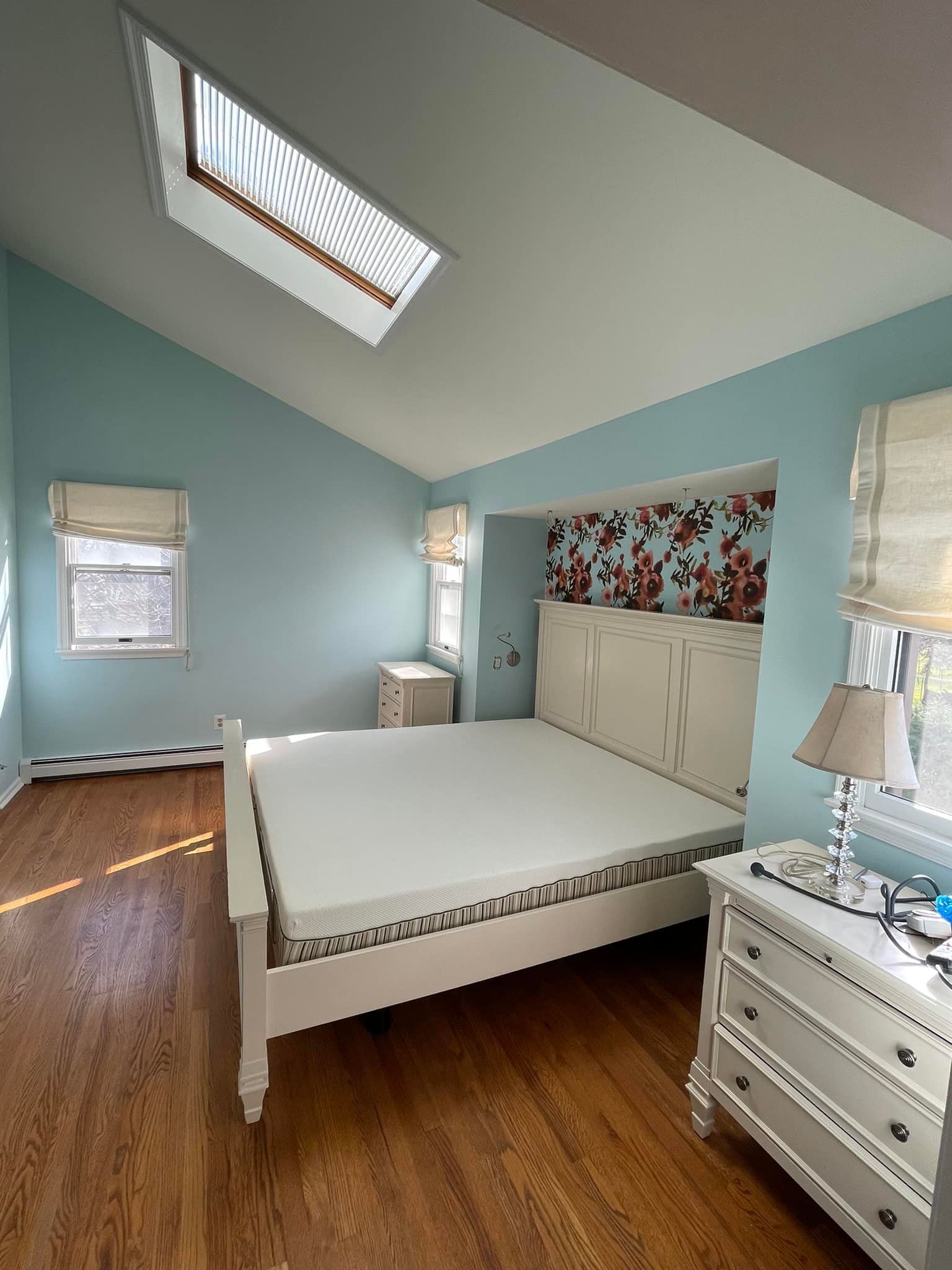Bedroom with white bed, blue walls, skylight, floral wallpaper, and wooden floor.