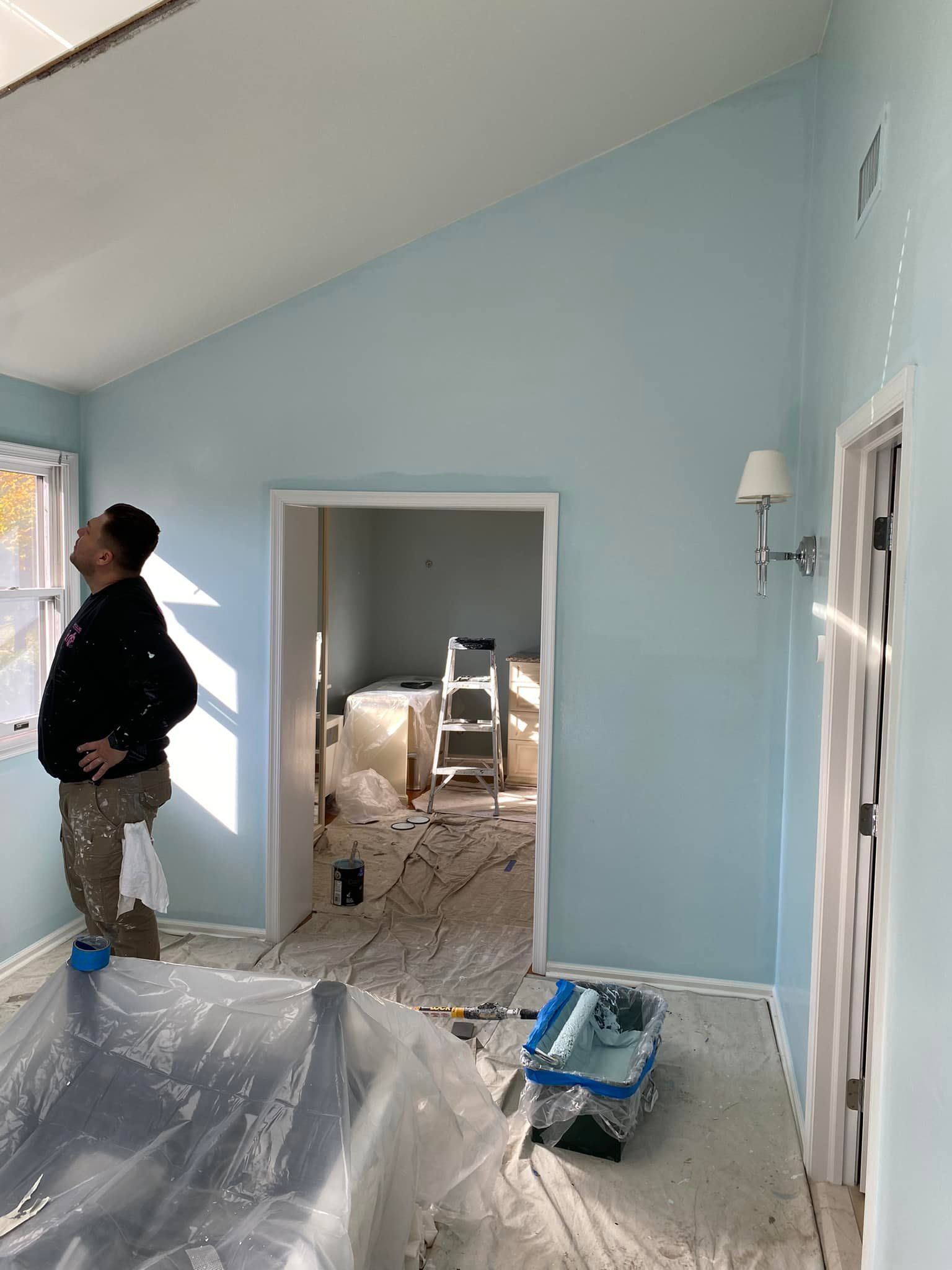 Person looking up at freshly painted blue wall in a room under renovation.