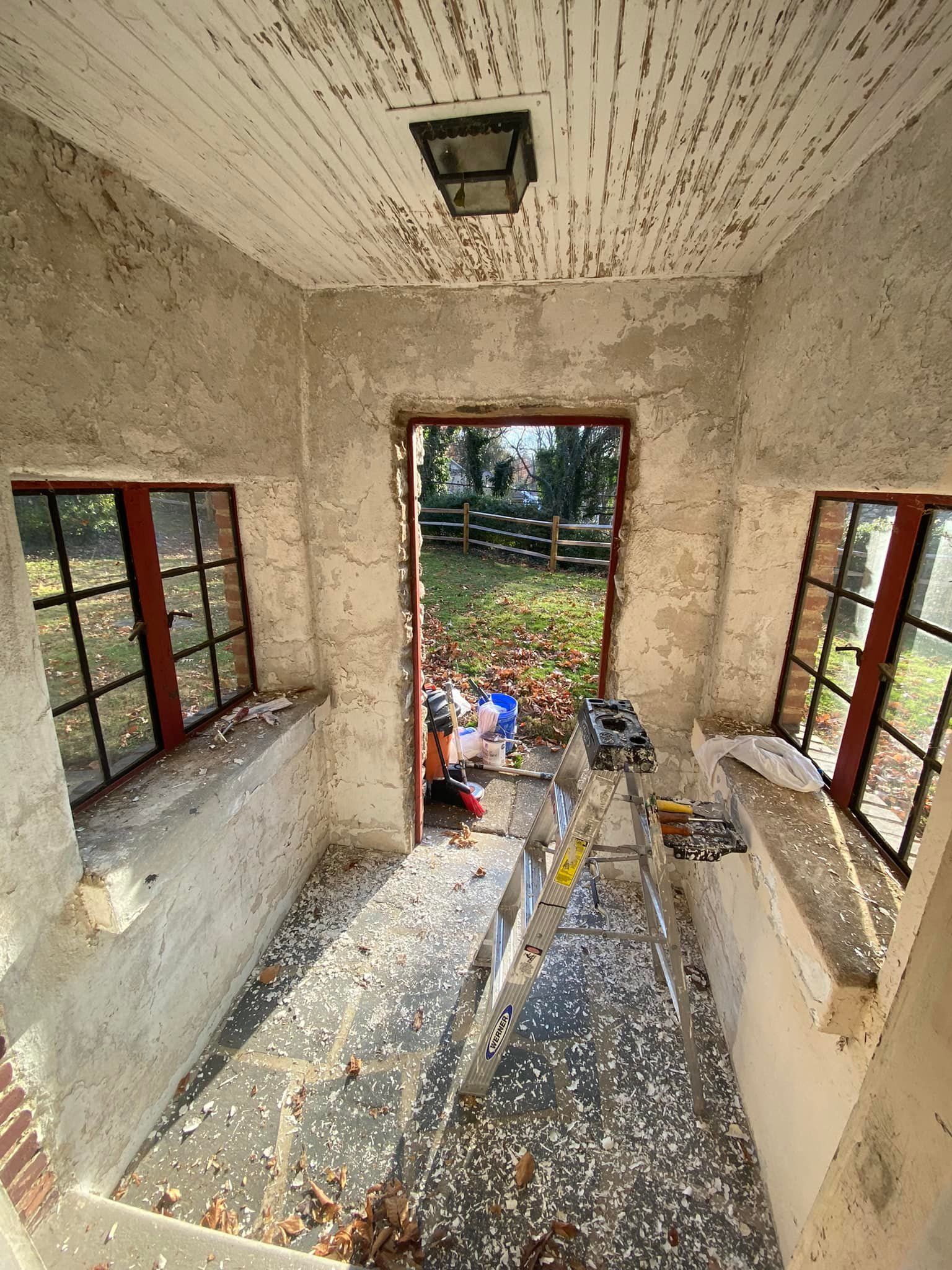 Interior of a room with two windows and an open doorway. The walls and ceiling are textured. Debris litters the floor.
